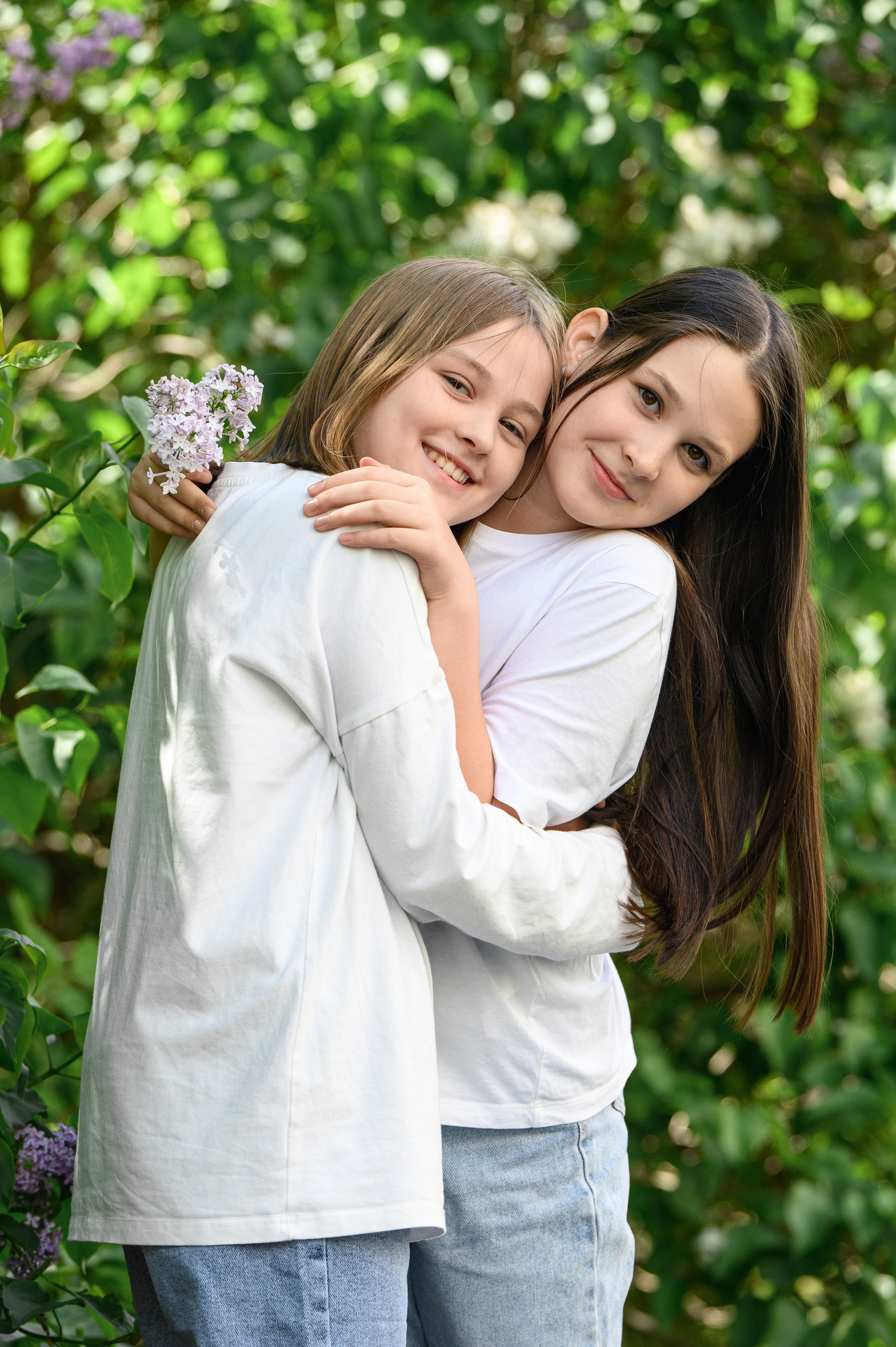 Две девочки обнимаются у кустов сирени