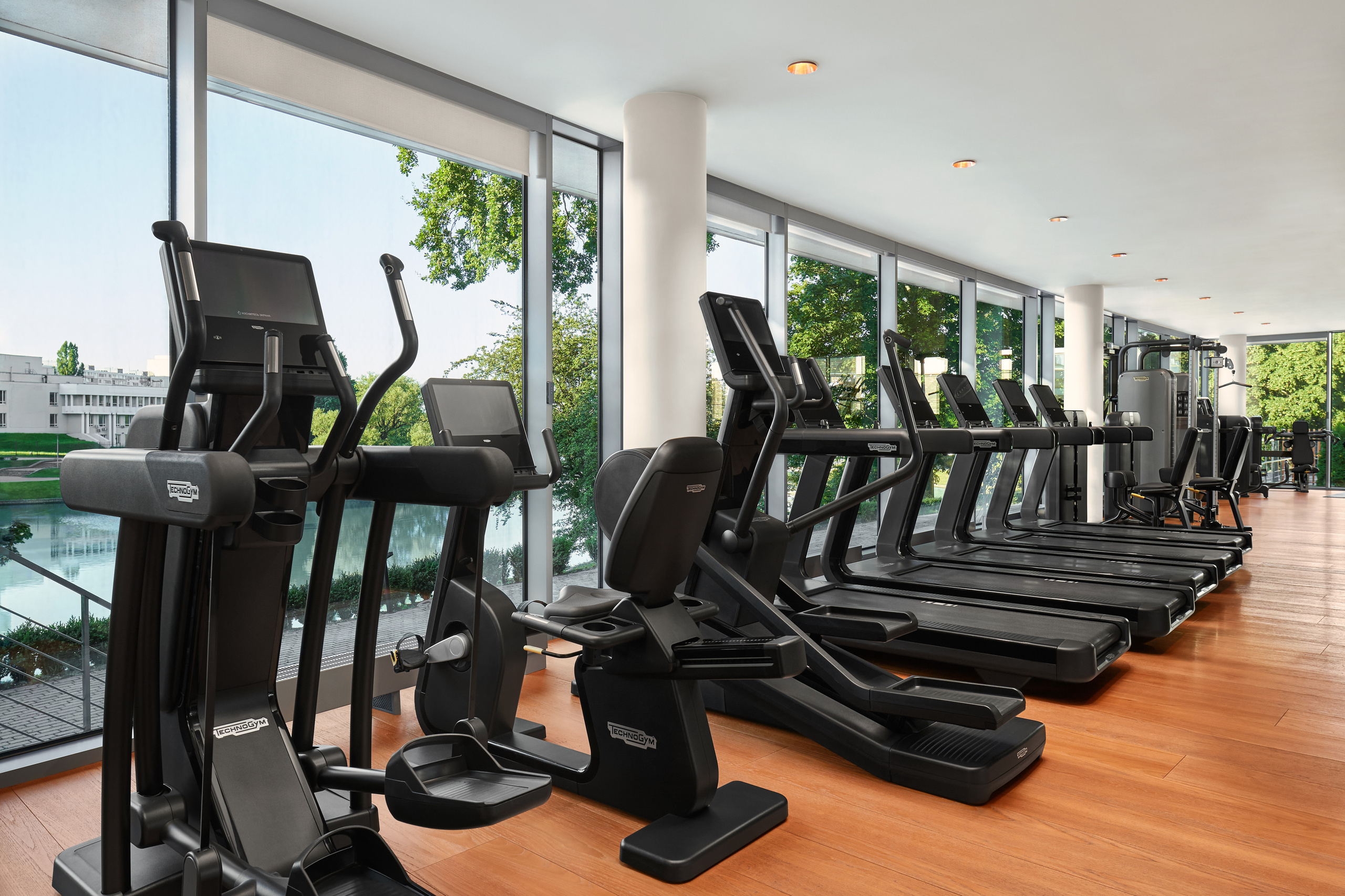 Фитнес, тренажеры, беговые дорожки, вид за окном, озеро, солнце 
