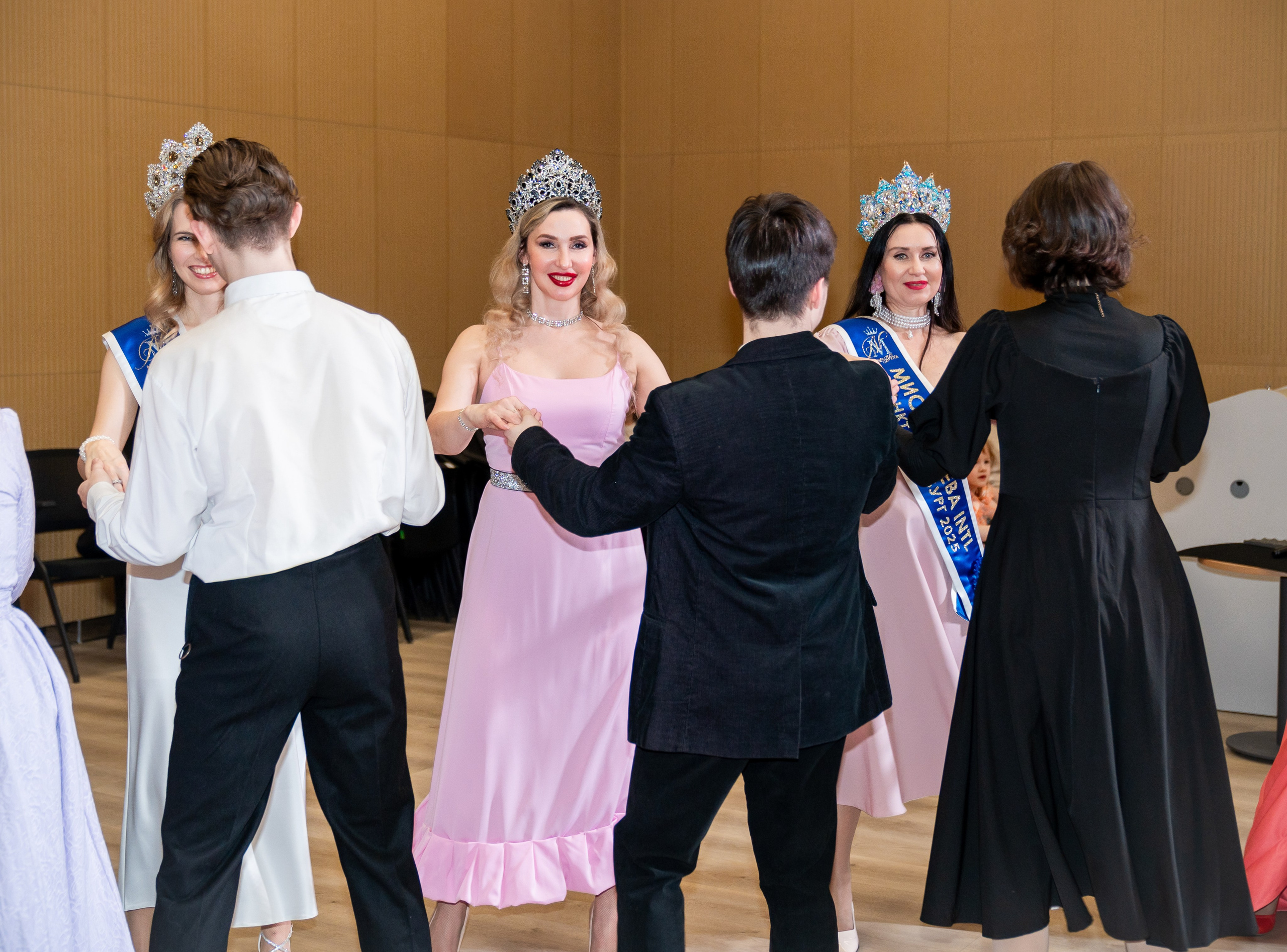 Участники инклюзивного бала «Мы все равны» танцуют в большом зале. Девушки в бальных платьях и коронах. Фотограф Мальцев Евгений.