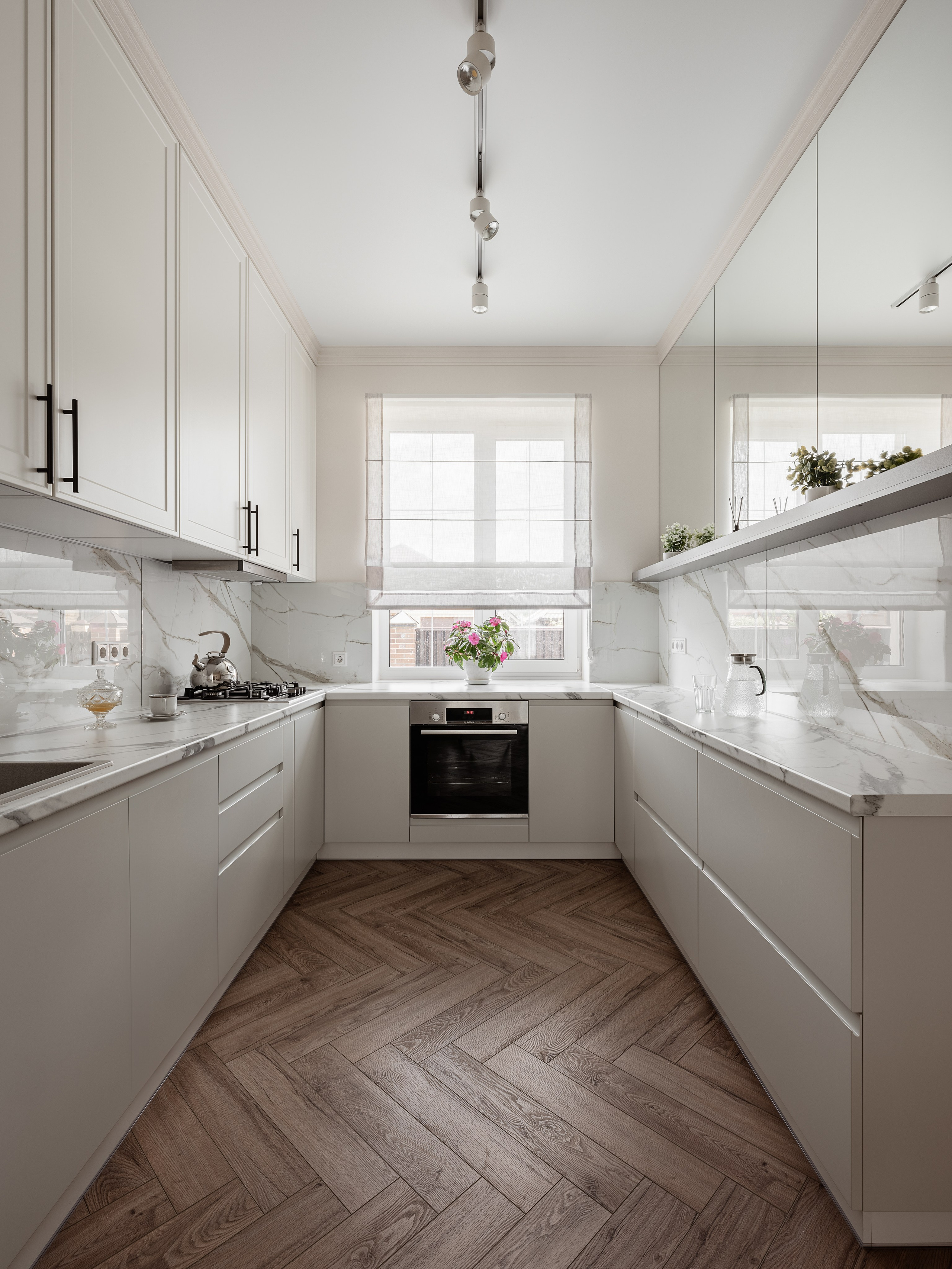 Функциональная кухня в светлых тонах с мраморными фасадами, встроенной техникой и деревянным полом елочкой. Интерьерная съемка от фотографа Сергея Денисенко, дизайн разработан Алиной Чередниченко.