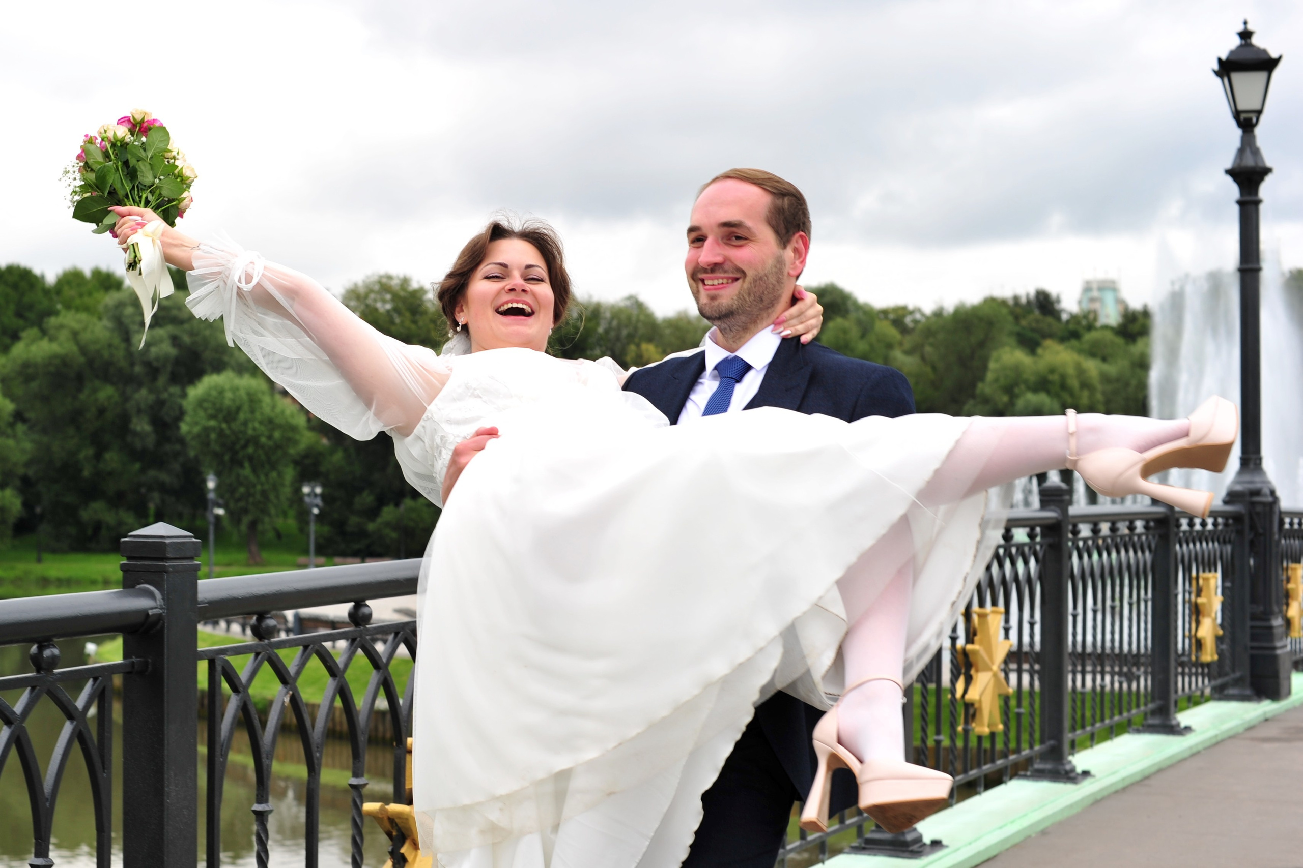 Свадьба в Царицыно пасмурным летним днем, жених несет невесту на руках по чугунному мосту через пруд, невеста размахивает свадебным букетом и кричит от радости