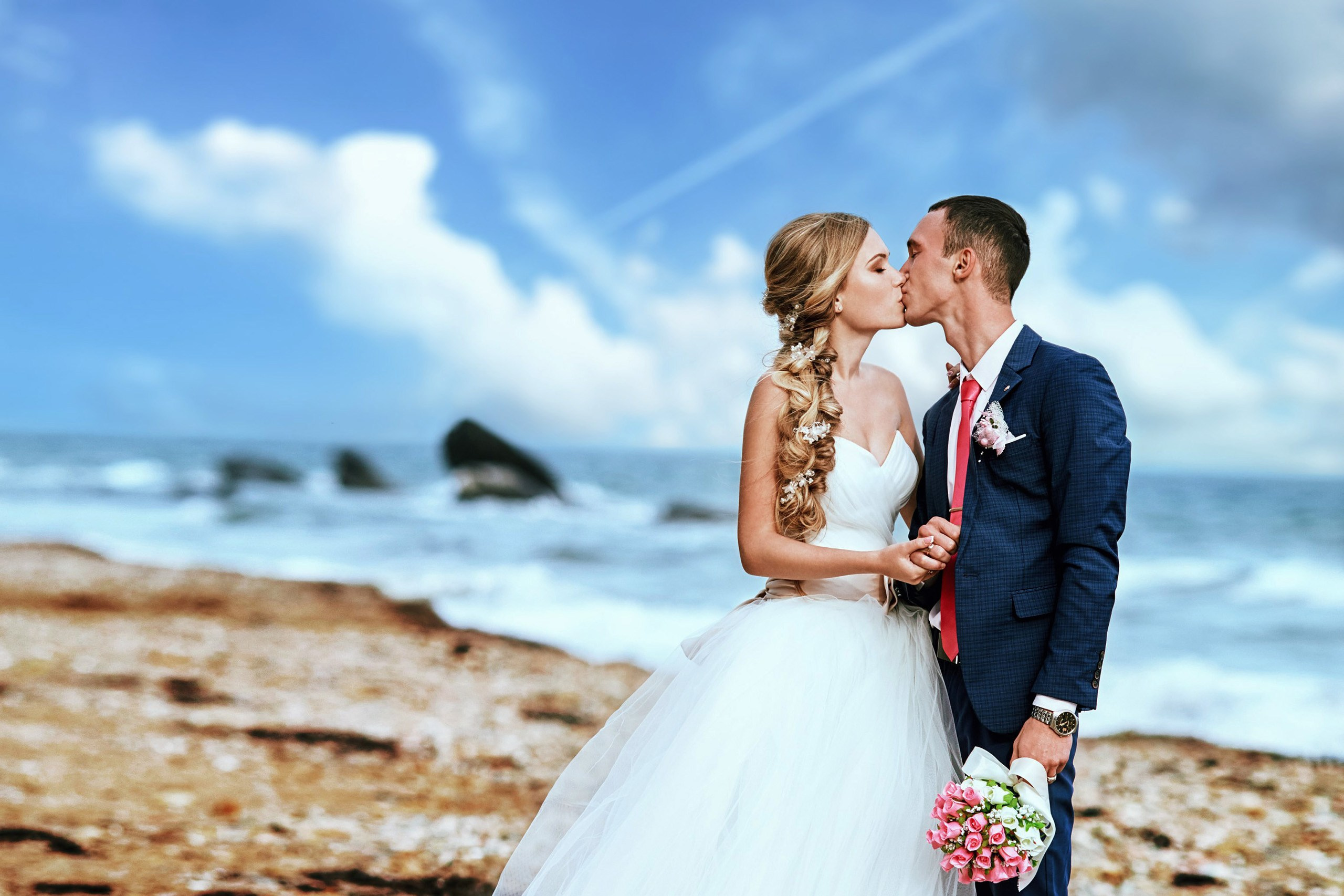 Свадебная фотосъёмка в Находке целующейся влюблённой пары на фоне моря, пляжа и белых облаков