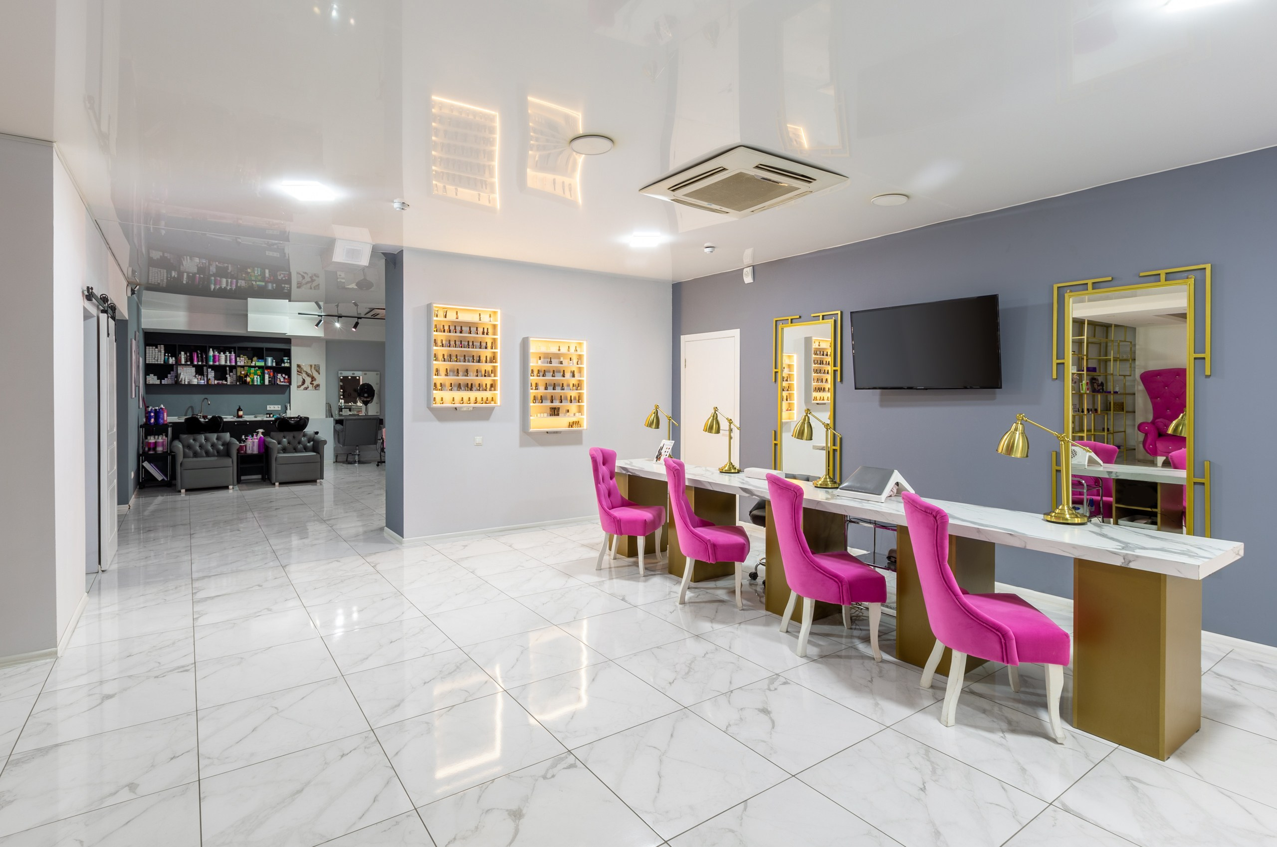 Косметология BEAUTY HALL GROUPP Воронеж. Места мастеров маникюра с мягкими розовыми креслами и длинным каменным светлым столом. Серые стены в интерьера косметологии.