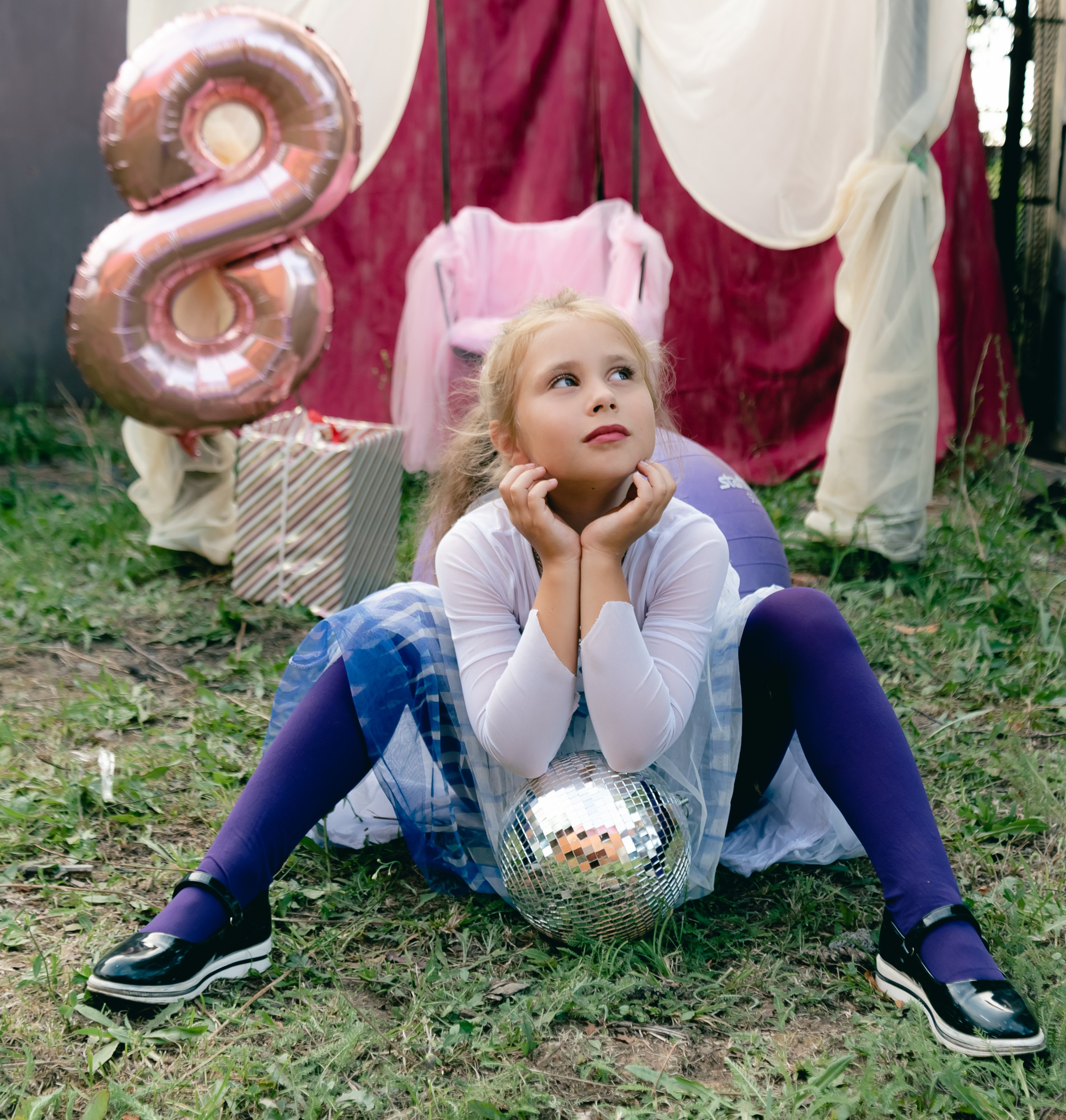 На фото девочка сидит облокотившись на шарик, ноги в сторону.