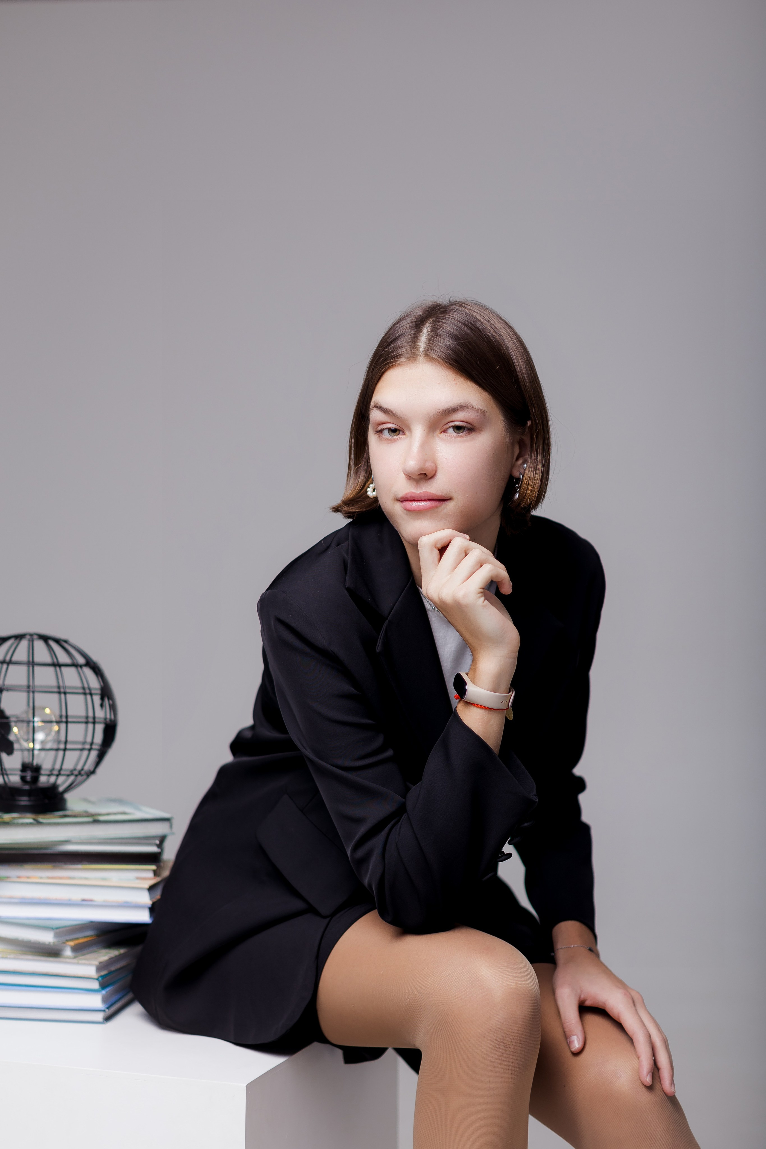 Девушка сидит на тумбе в фотостудии с глобусом на нейтральном фоне