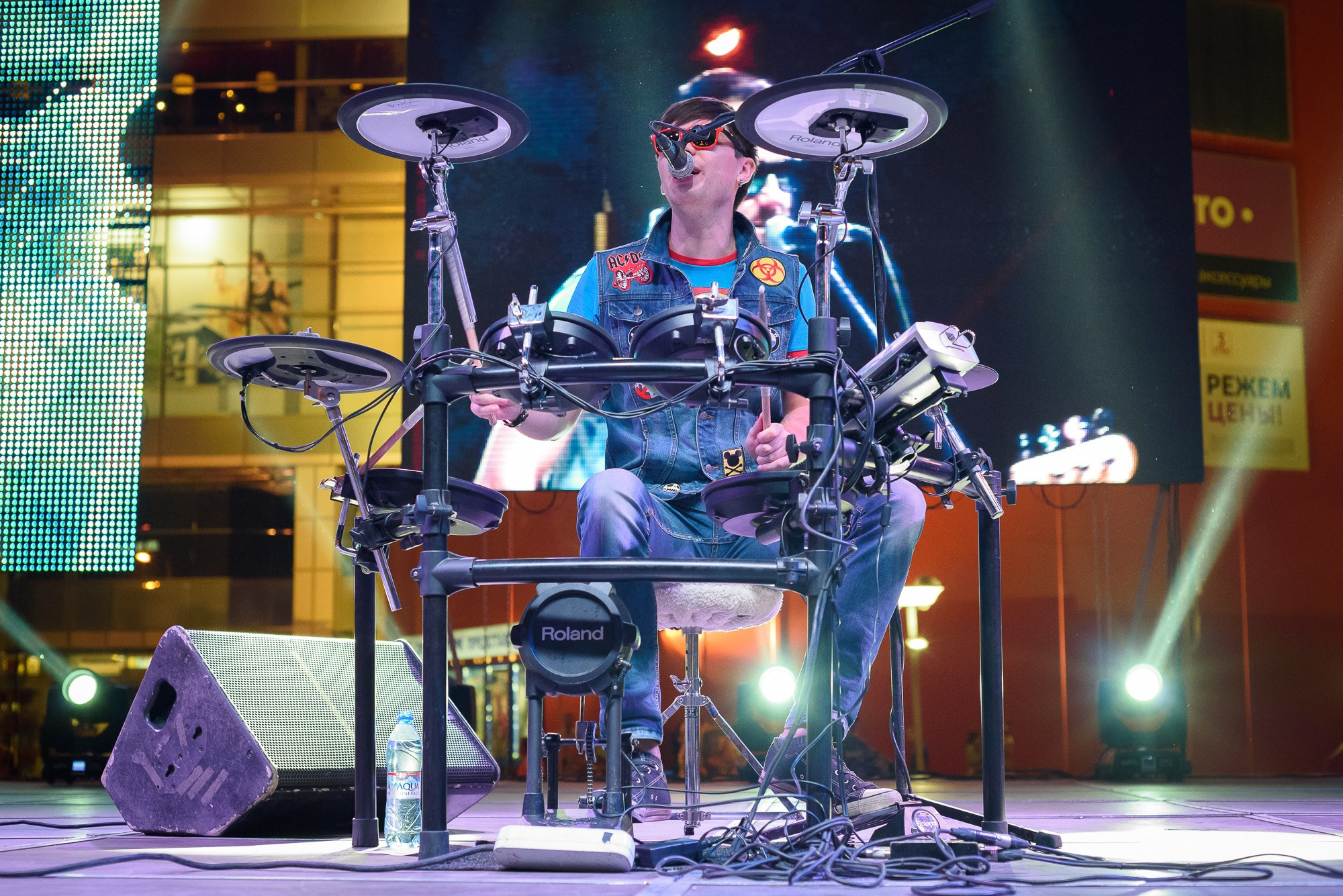 Барабанщик группы Staffles в красных очках сидит за барабанной установкой и поёт песню
