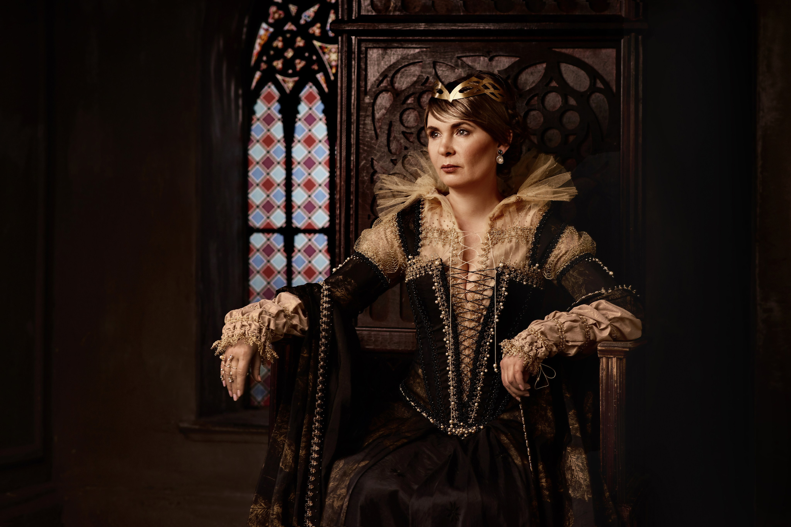 Историческая фотосессия женщины в средневековом черно-золотом костюме XVI века на троне в замке