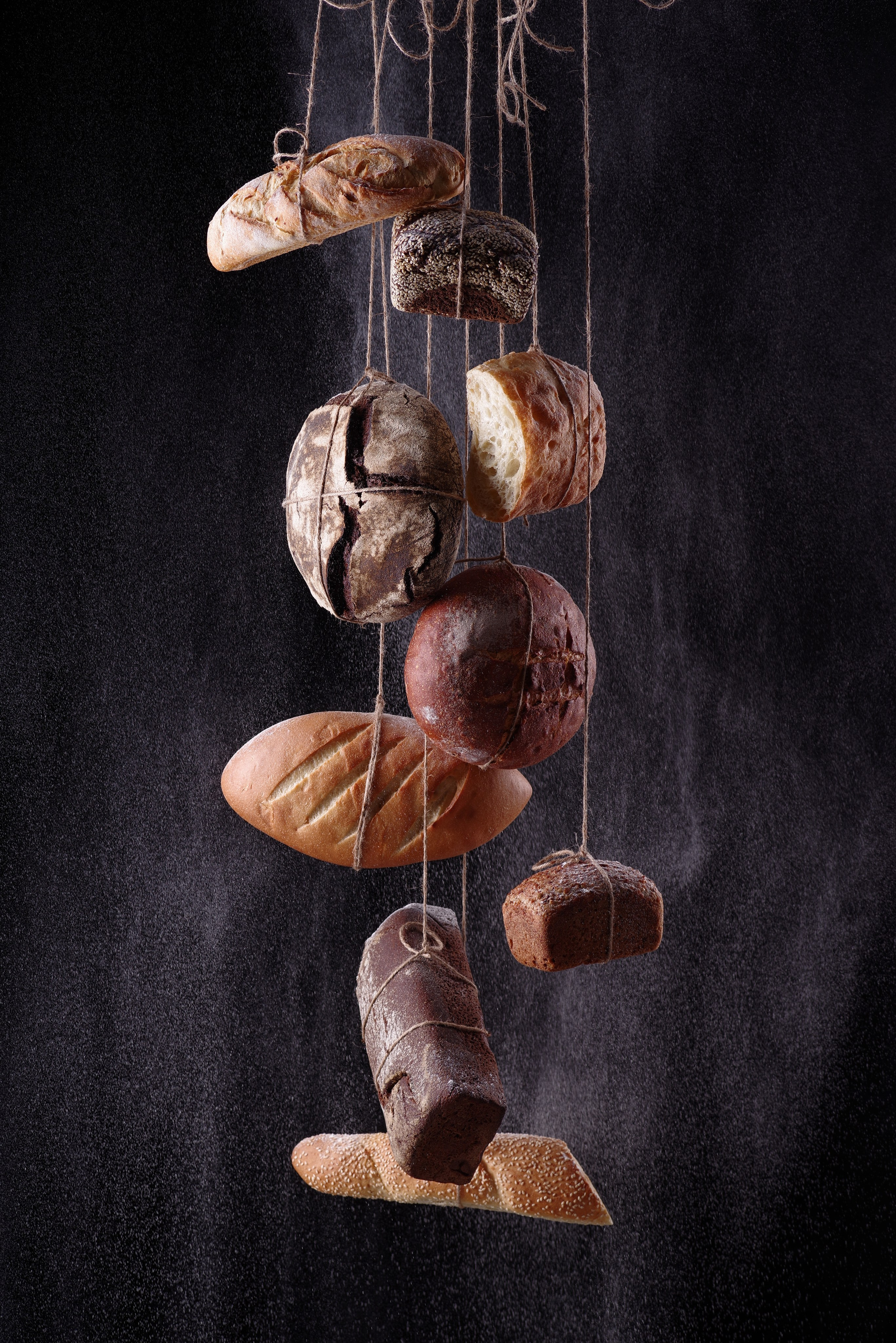 Разные виды хлеба на верёвочках на чёрном фоне 