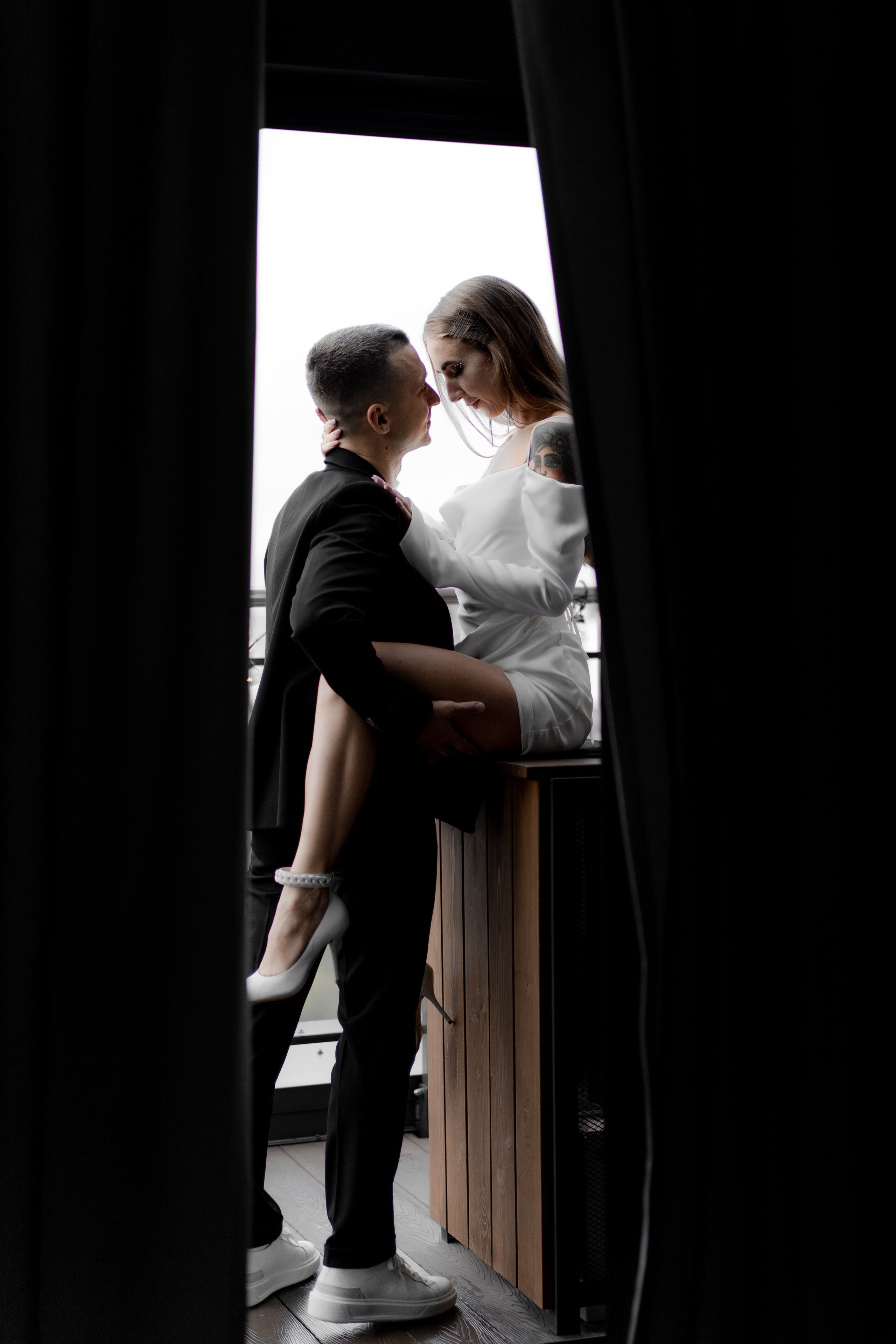 Невеста сидит на столе, жених стоит перед ней и обнимает