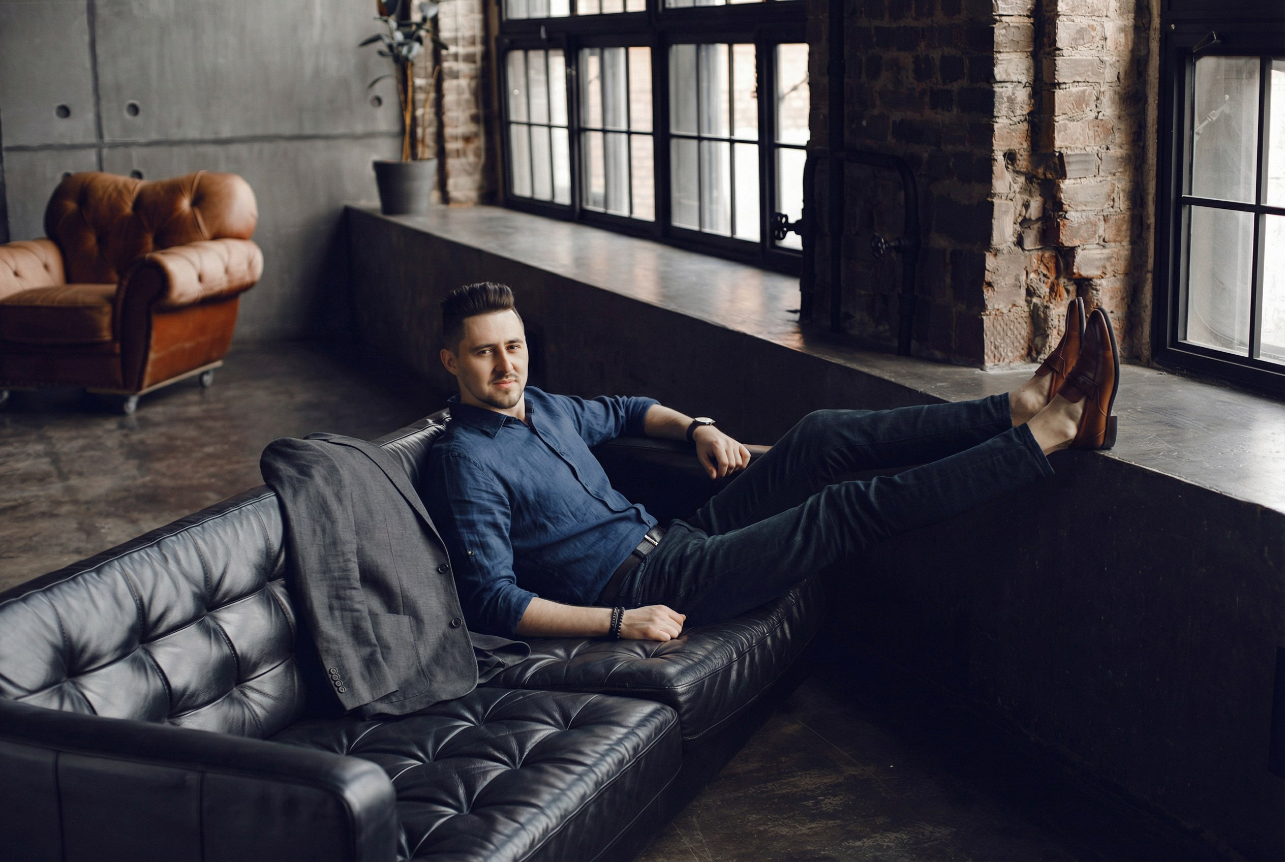 Мужчина в casual-одежде сидит на диване в интерьере лофт-студии.