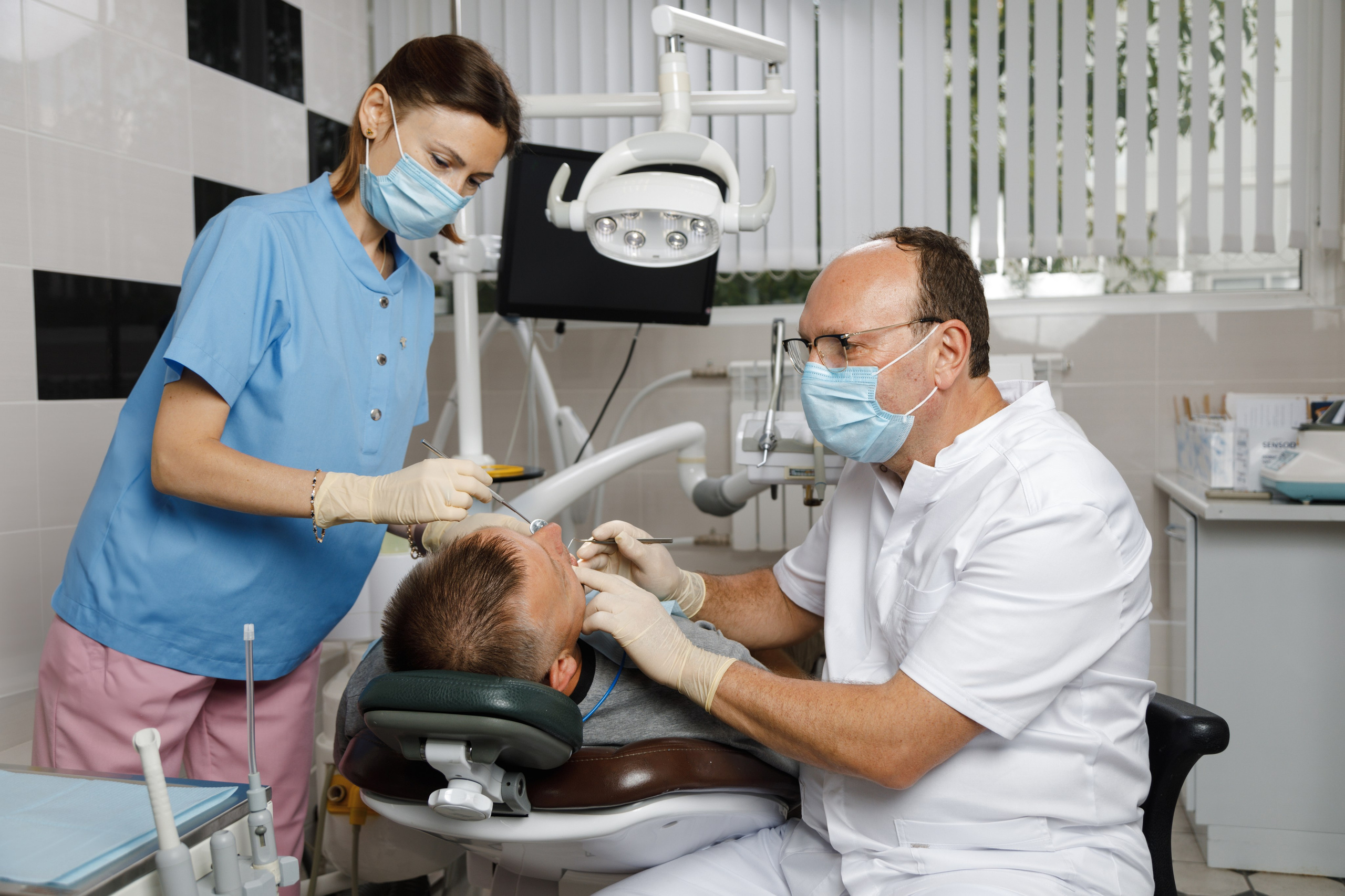 Процесс лечения зуба: стоматолог и медсестра работают с пациентом в современном кресле.
