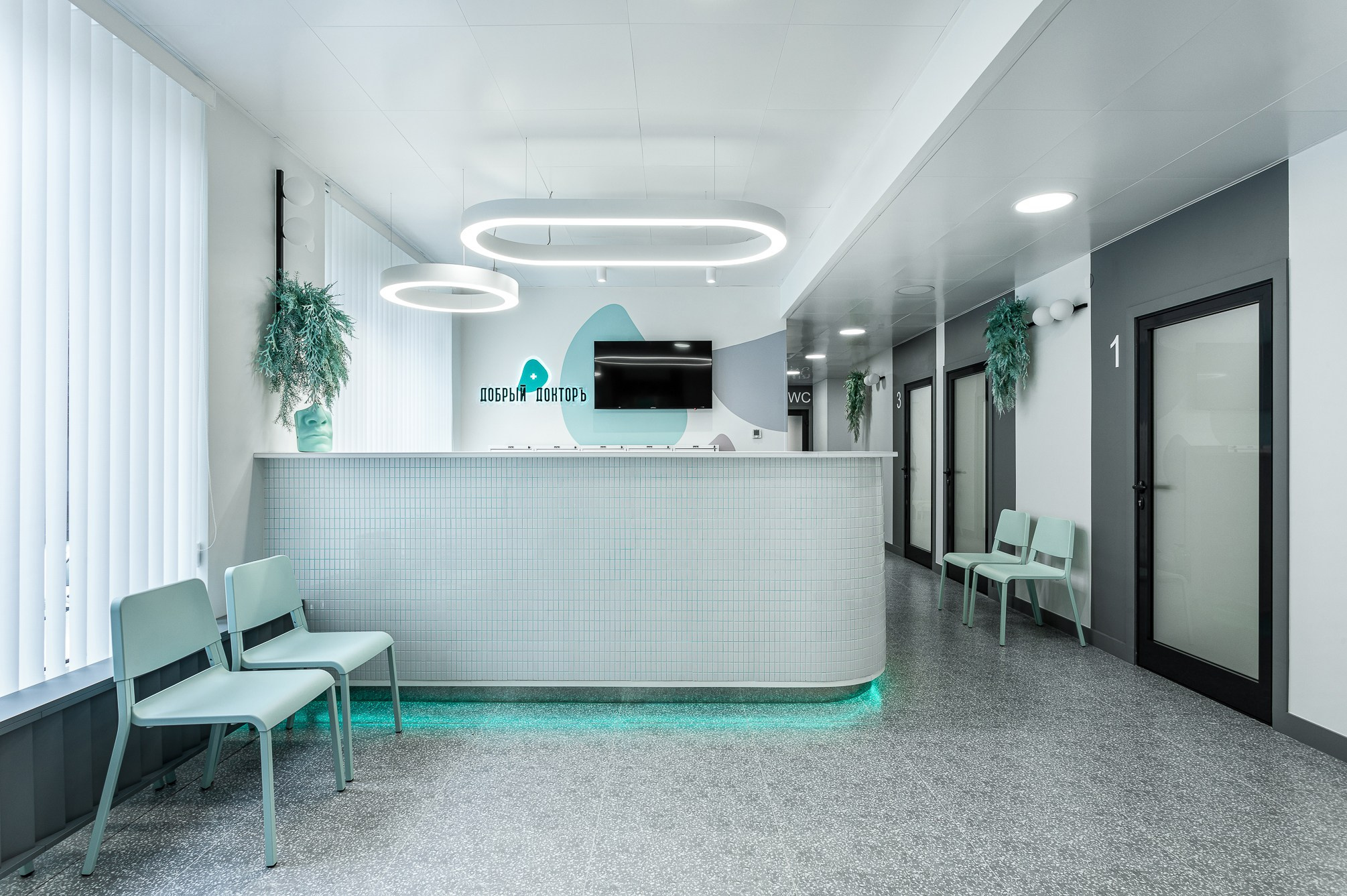Ресепшен семейной клиники с голубой подсветкой и продолговатой люстрой.
