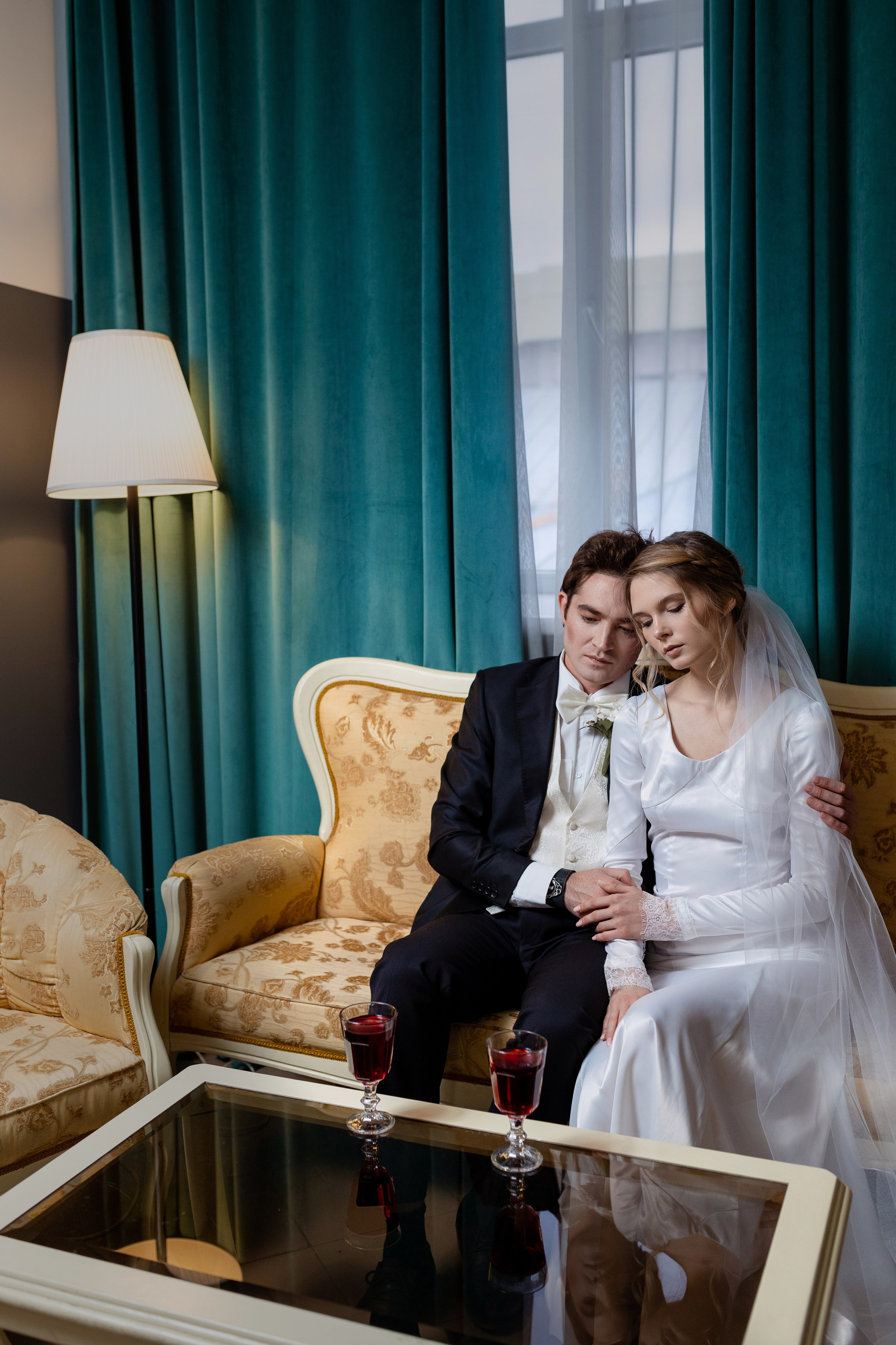 Жених с невестой сидят на диване, сбоку светится торшер.
