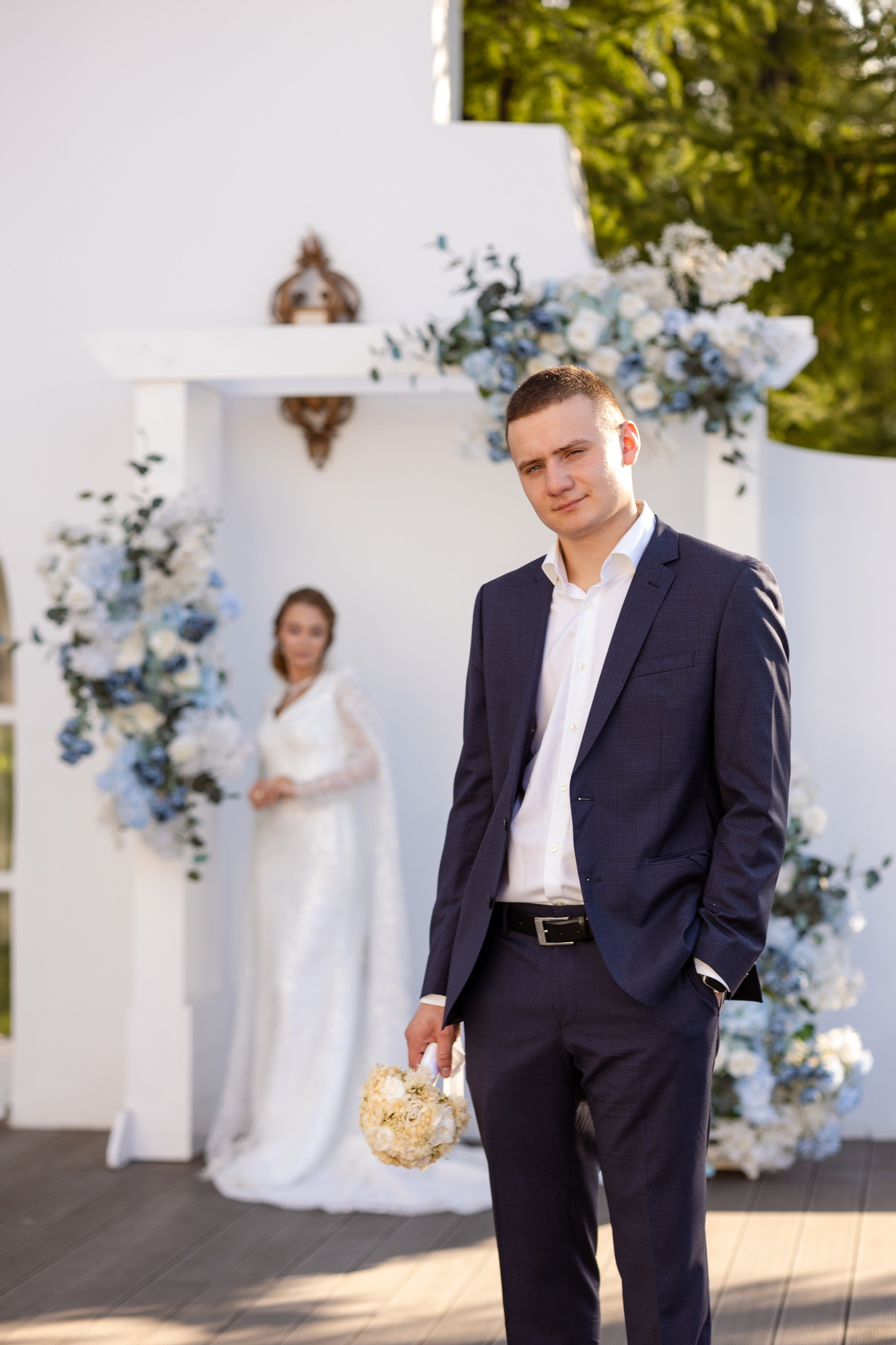 Невеста на заднем плане у белой стены.