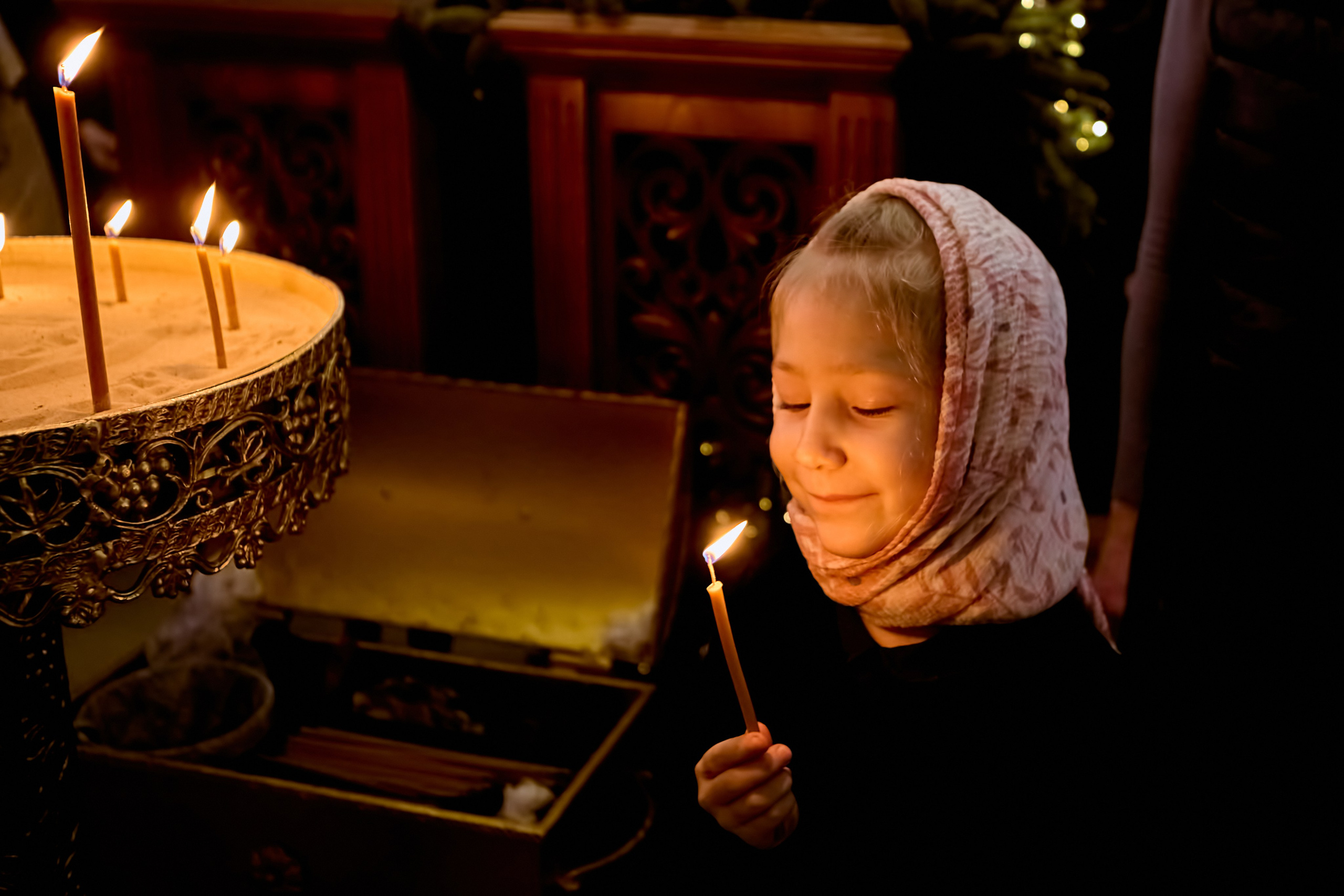 Маленькая девочка, 6 лет, держит зажженную свечу и радостно смотрит на нее