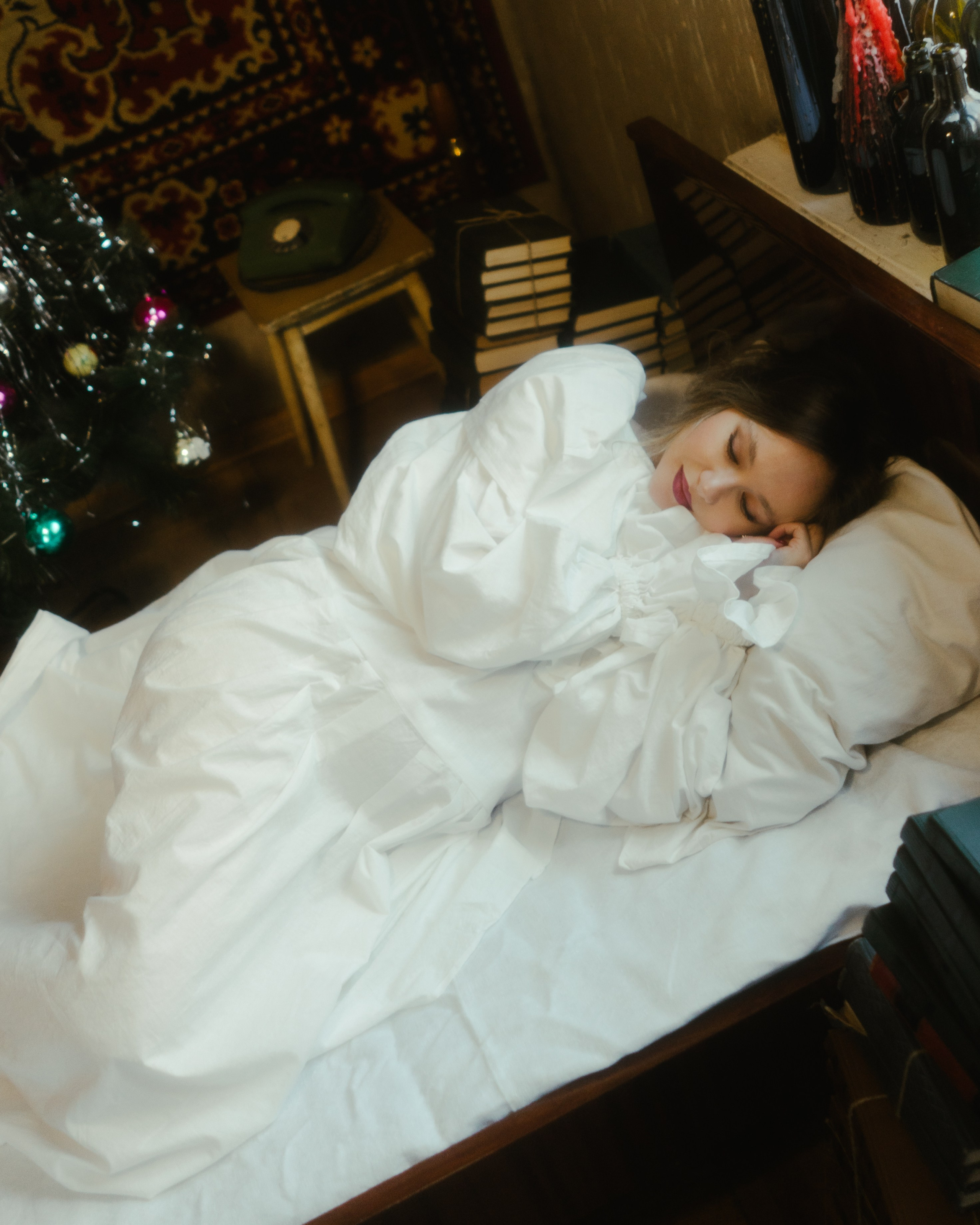 Будуарная фотосессия беременности: беременная в белых простынях на кровати рядом с новогодней елкой, теплый ретро-свет, фотостудия Санкт-Петербург.