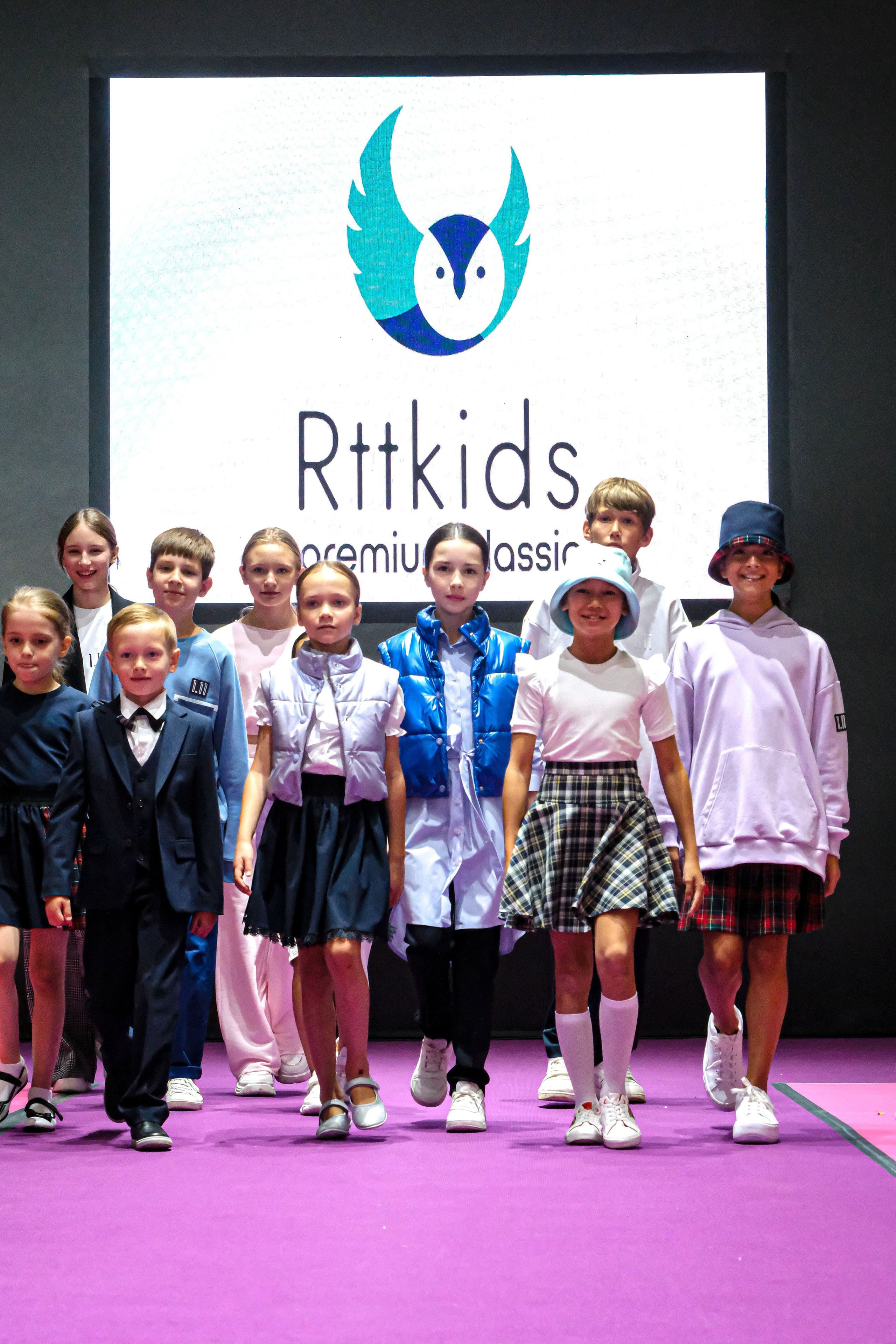  "Модели в ярких нарядах проходят по подиуму во время показа мод, освещенные яркими софитами и окруженные восторженными зрителями."