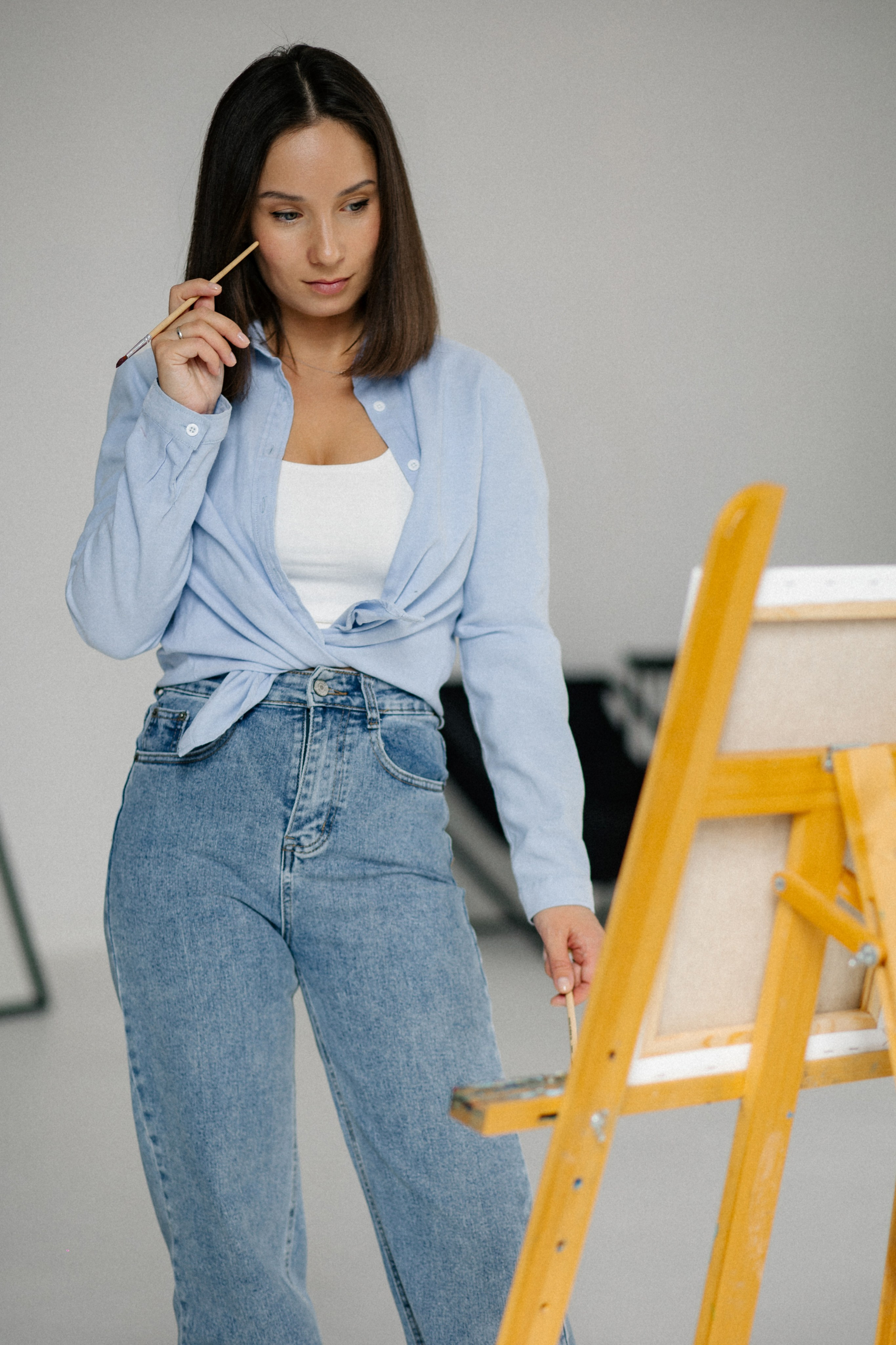 красивая, задумчивая девушка с кисточками  перед мольбертом 