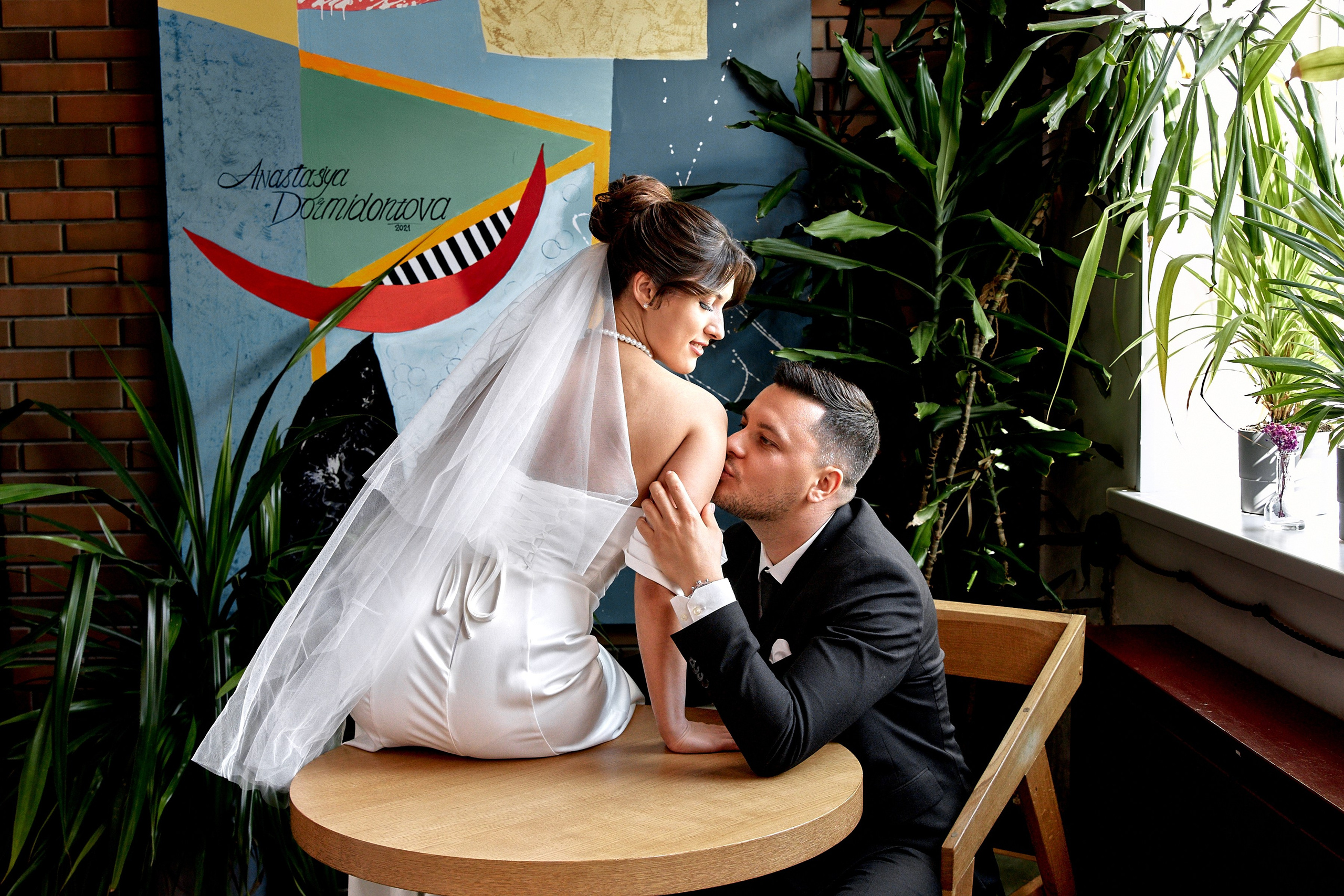 Свадебная фотография в кофейне — жених целует невесту в плечо. Естественные эмоции молодоженов в интерьере заведения. Лучший свадебный фотограф России Елена Орешина.