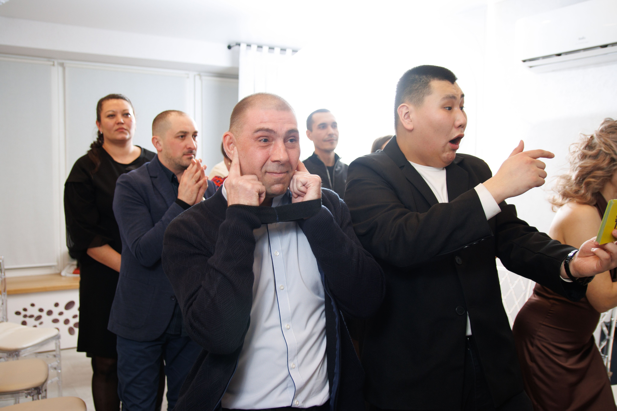 Мужчина изображает забавное выражение лица, вокруг смех гостей.