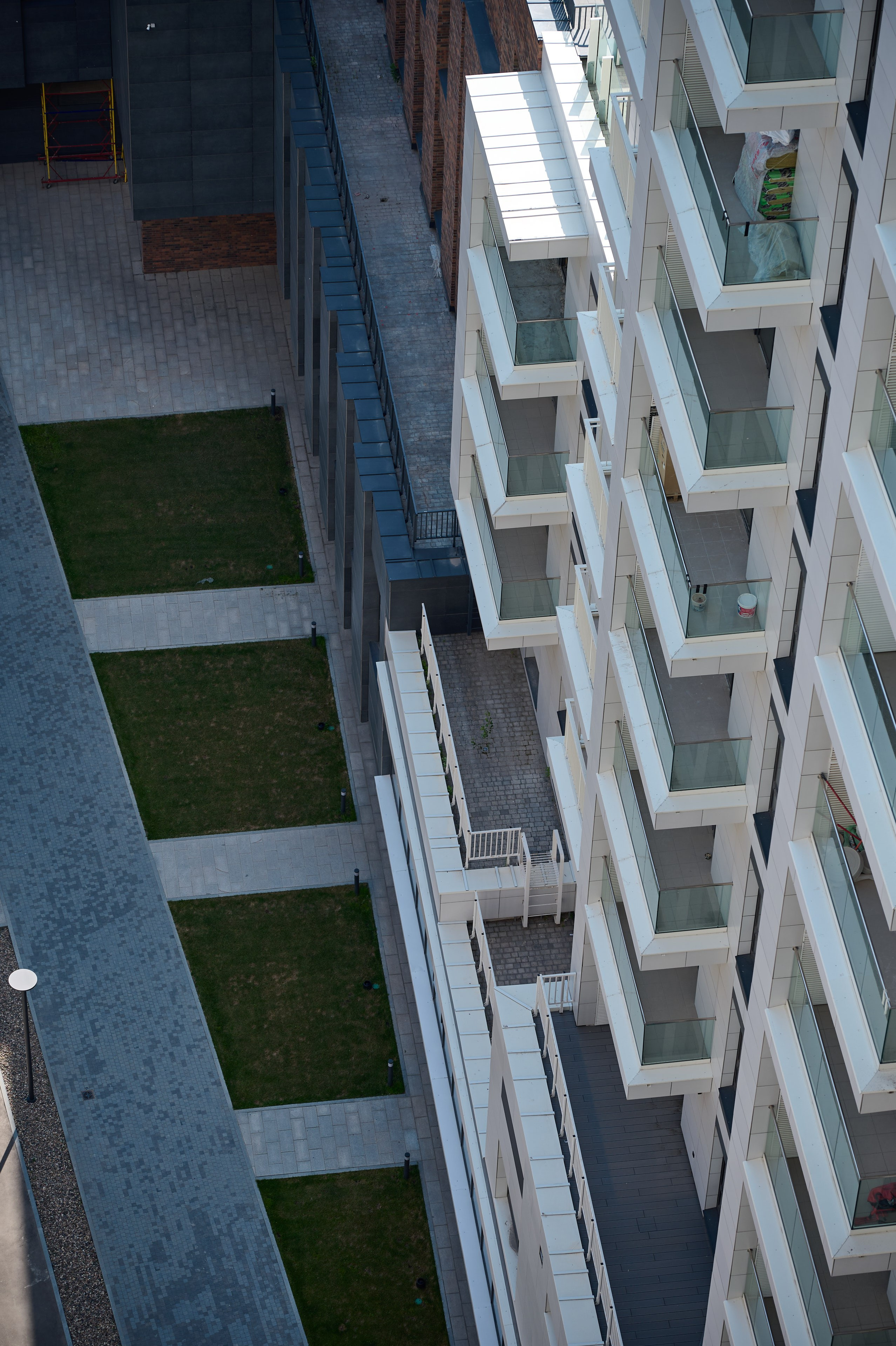 Вид сверху на внутренний двор жилого комплекса с газонами и бетонными дорожками между светлыми фасадами зданий с балконами