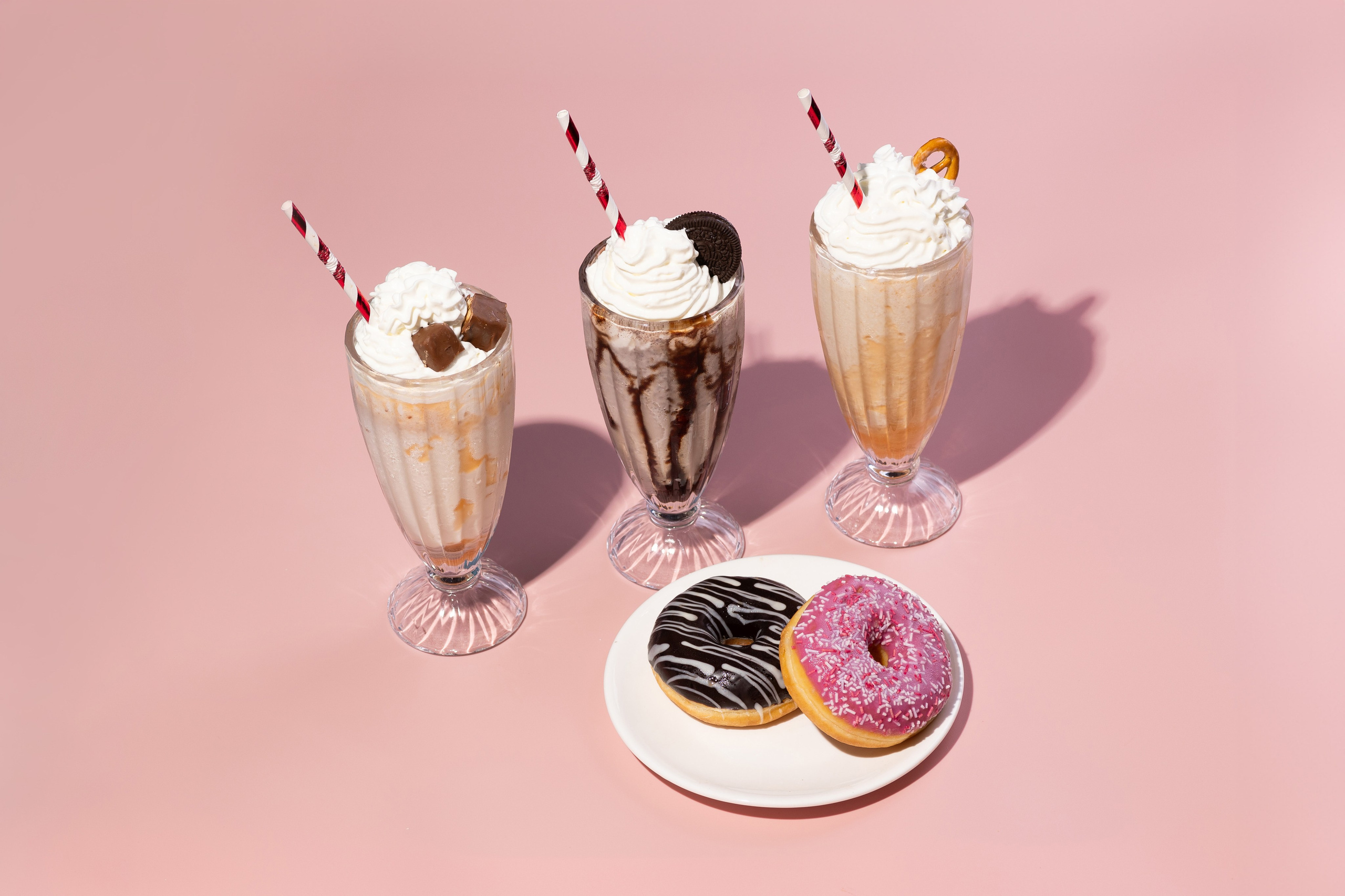 Три молочных коктейля с пончиками в тарелке на розовом фоне