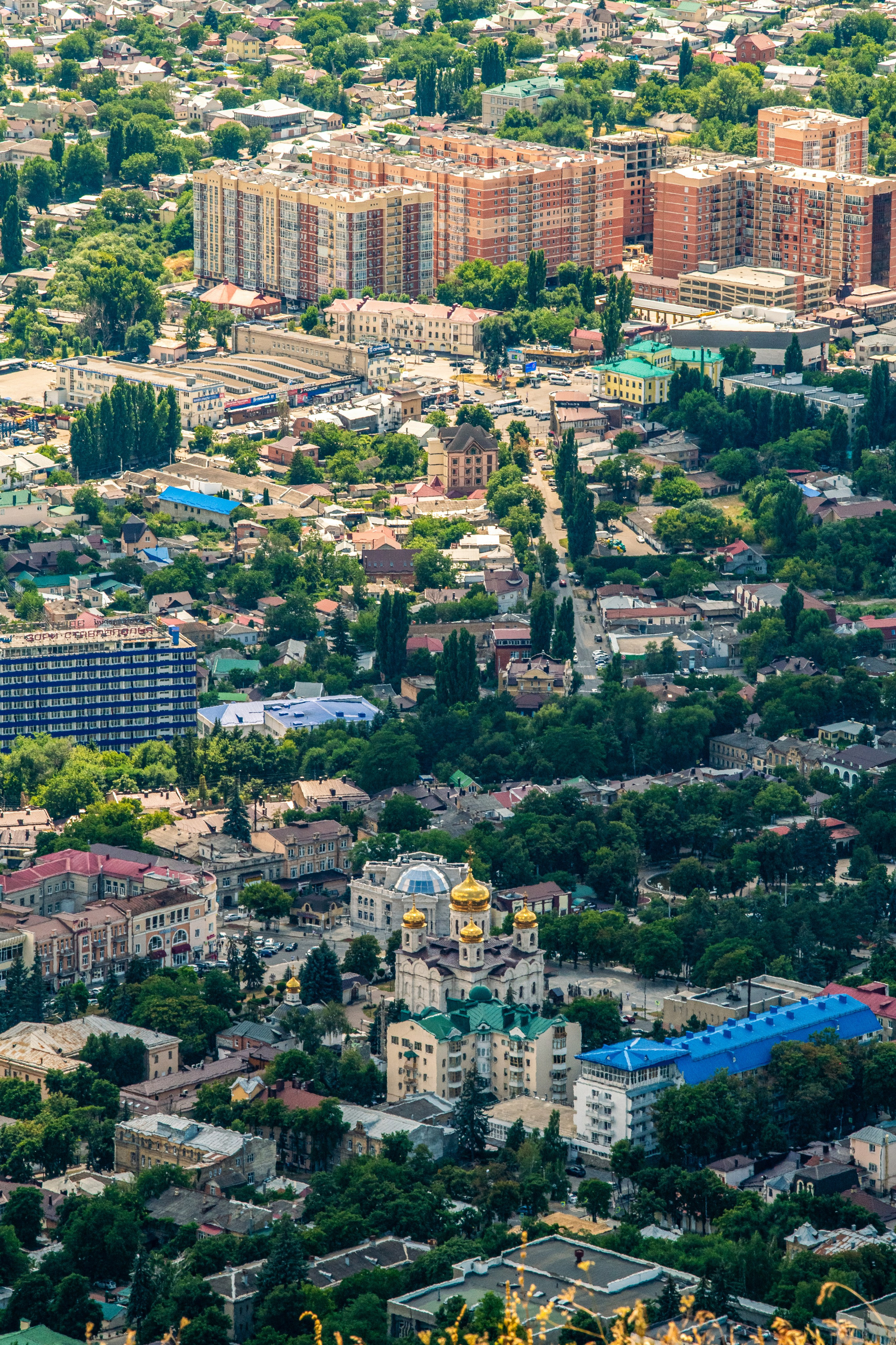 На изображении виден городской пейзаж Пятигорска с множеством зданий, деревьев и дорог. В центре — церковь с золотыми куполами