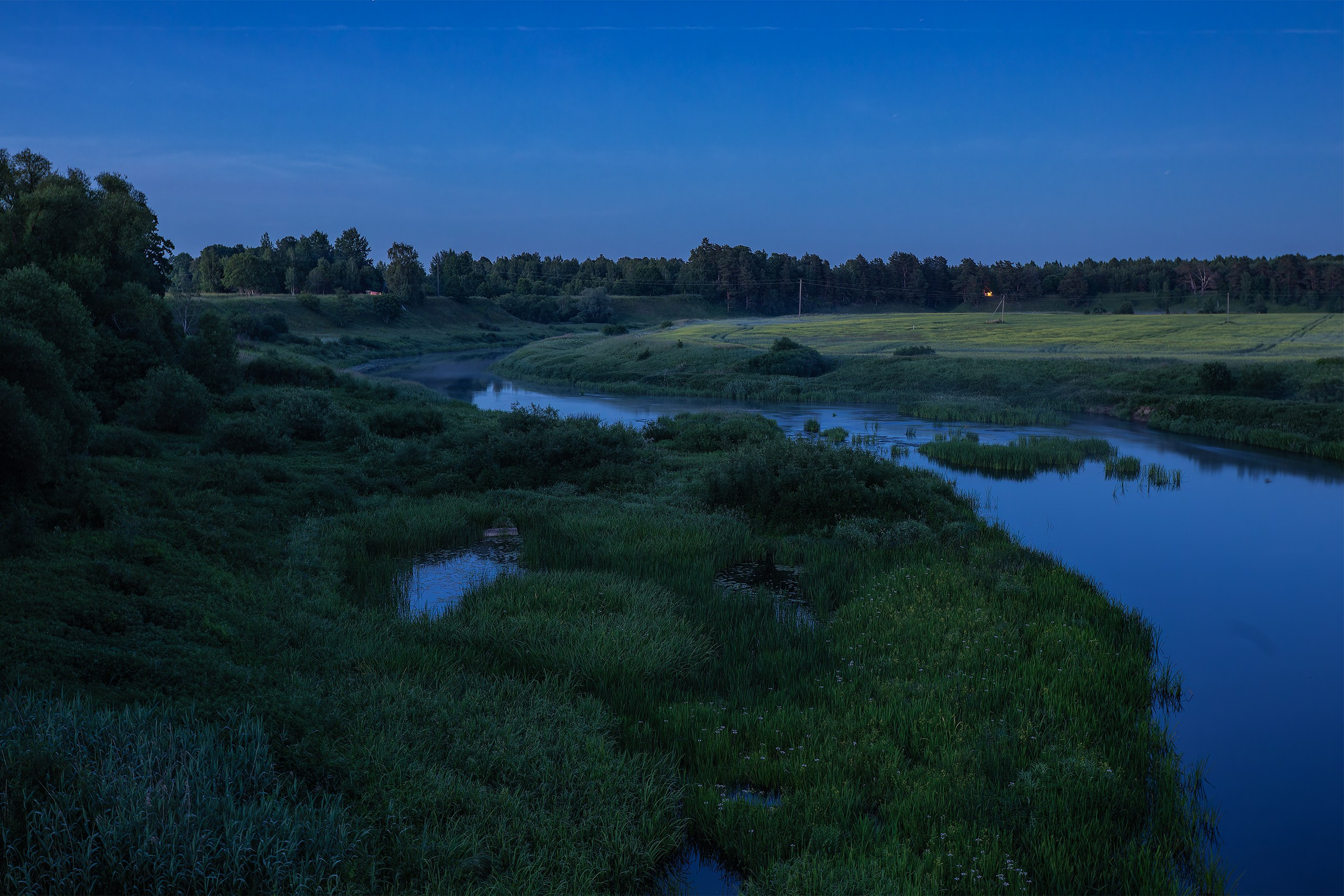 The winding Sheshupe River and grassy wetlands seen in deep blue twilight in East Prussia.