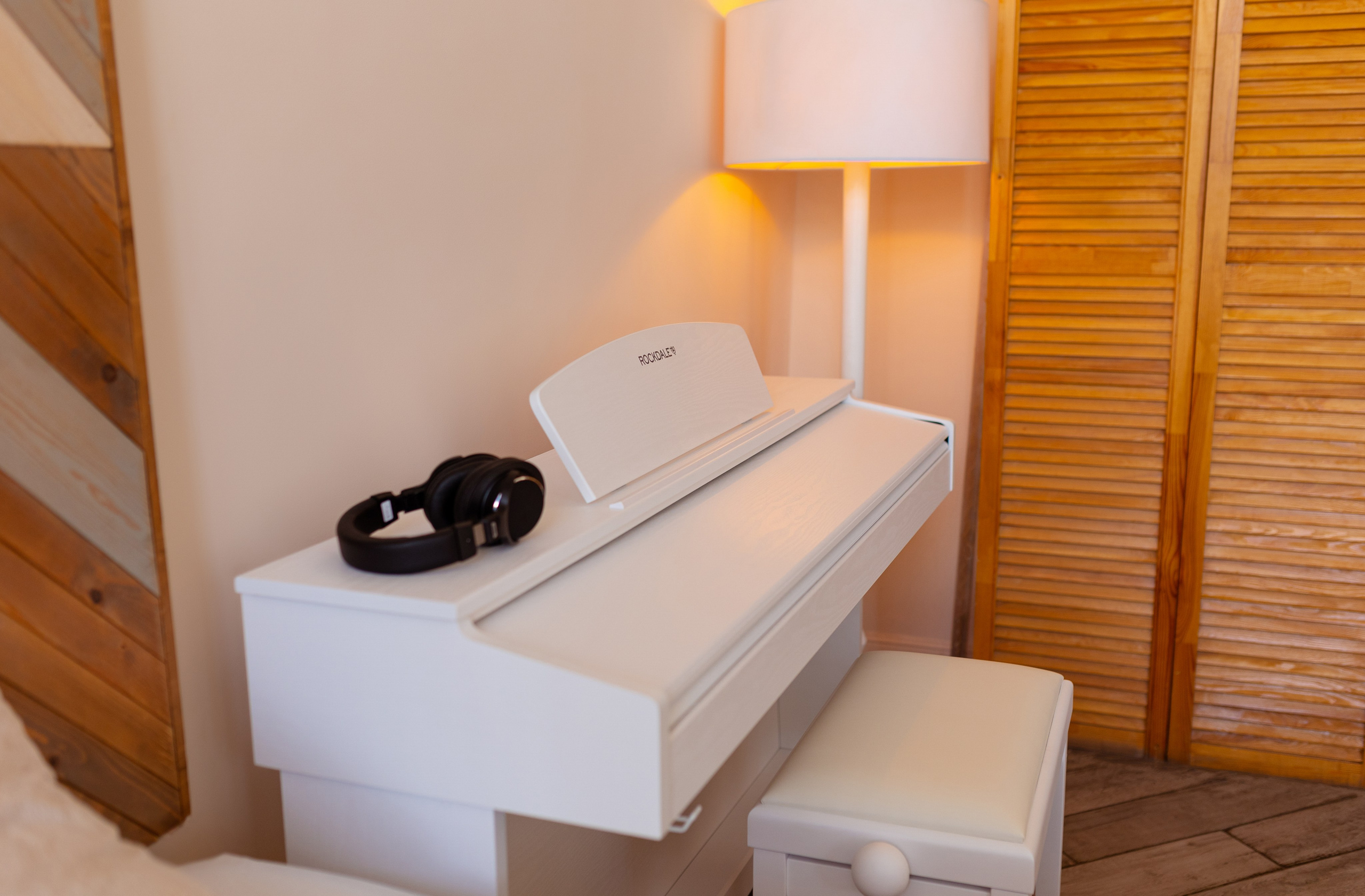 Белое пианино, белый табурет на фоне белого торшера.