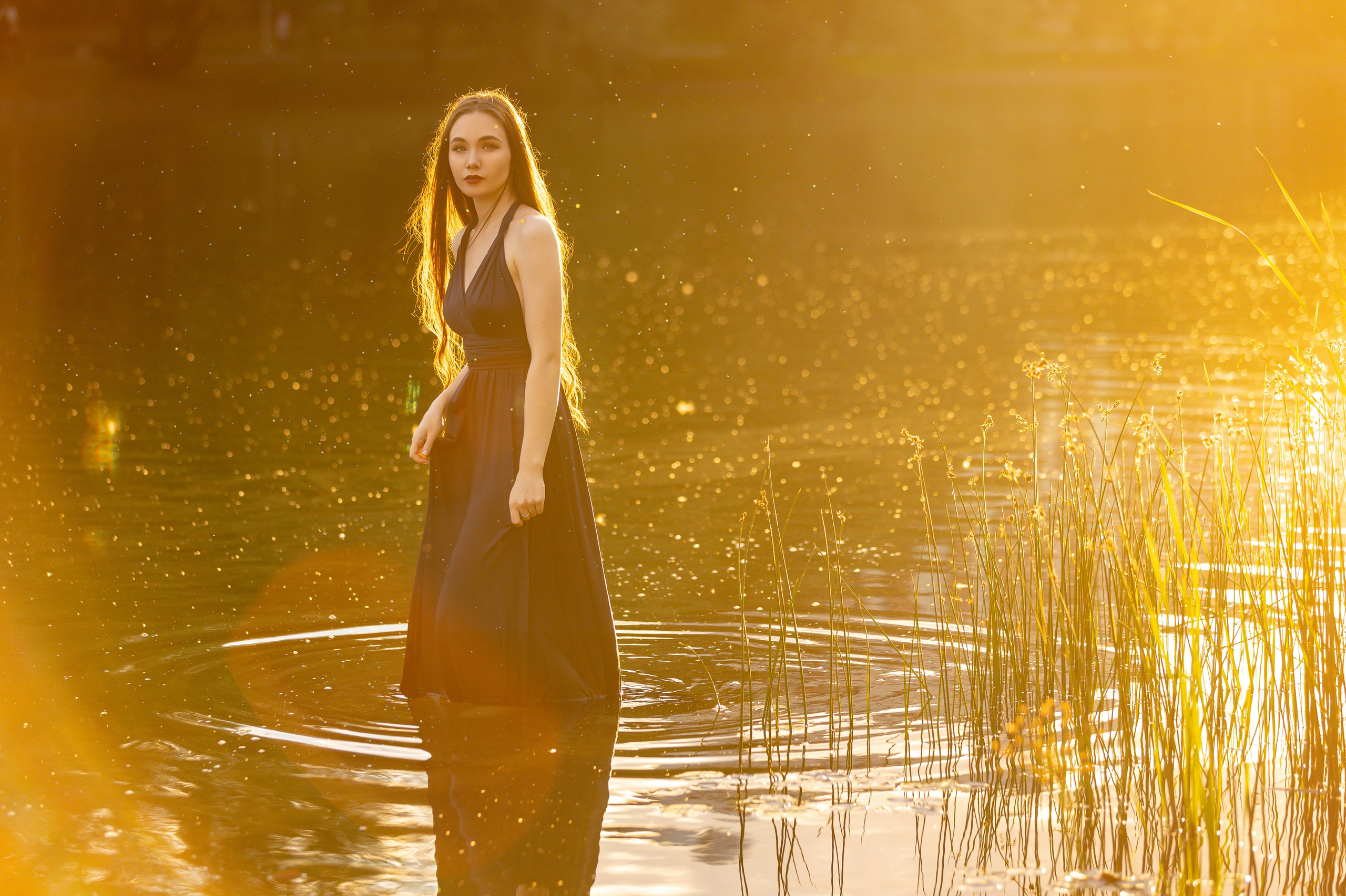 Девушка в лучах закатного солнца стоит в пруду с кувшинками