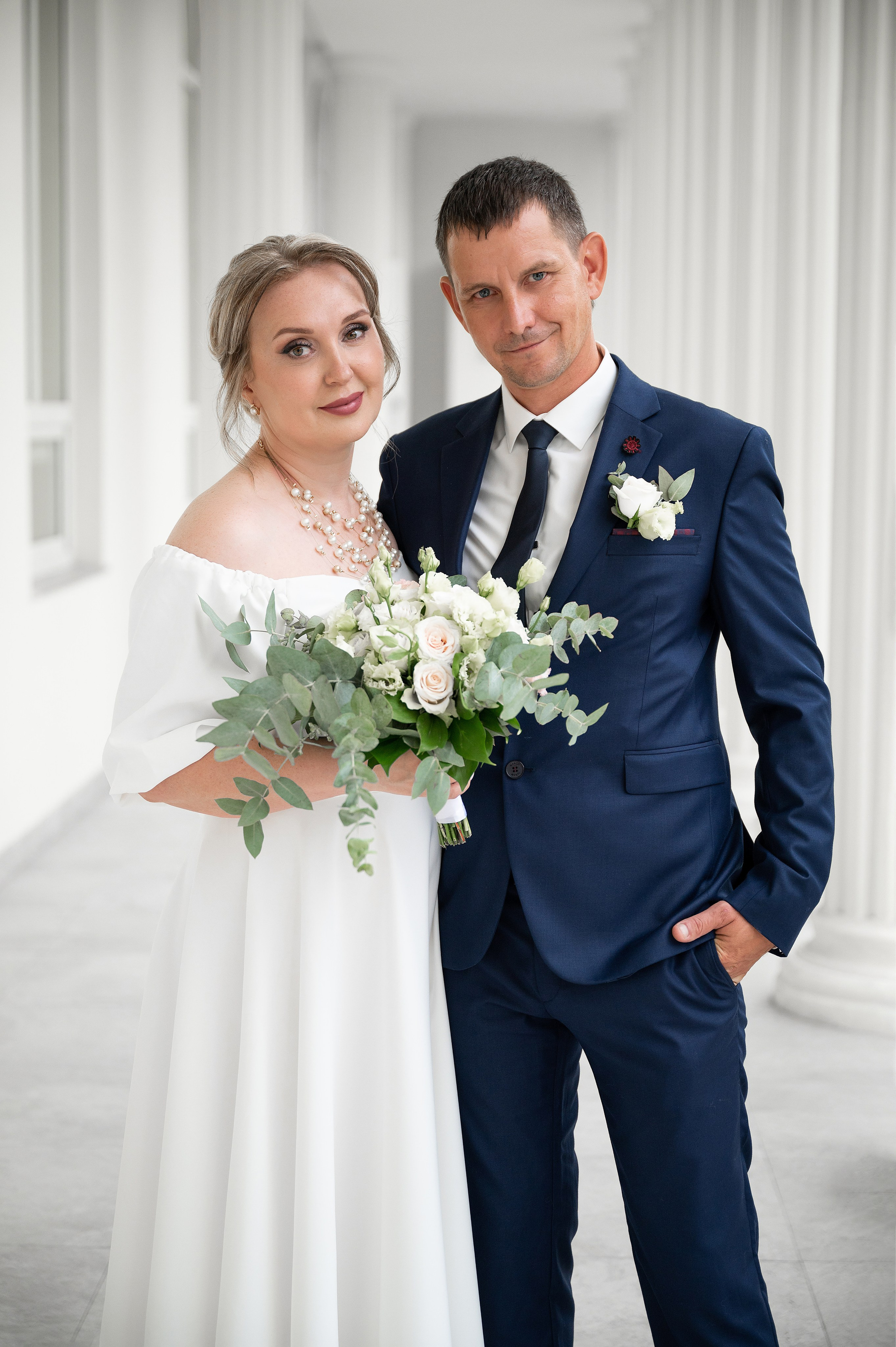 Жених обнимает невесту на фоне белых колонн в Краснодаре