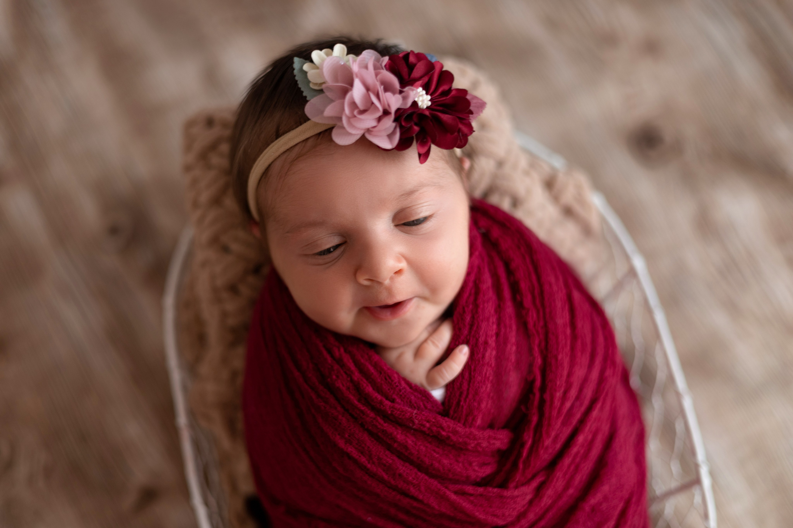 новорожденная девочка в бордовом наряде в белой корзинке