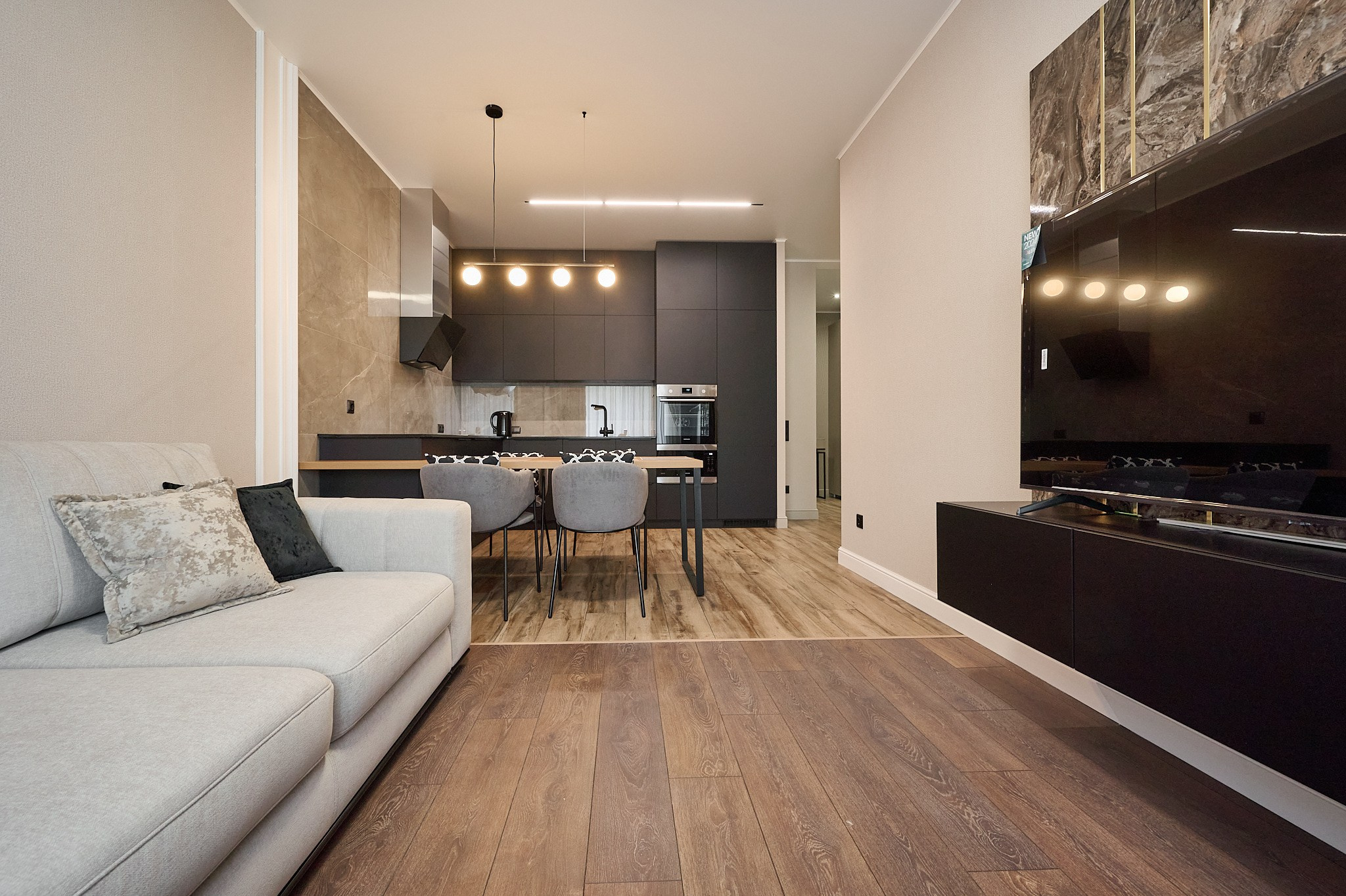 кухня светлый диван черная полка телевизор черные шкафы и полки светлый стол серые стулья 