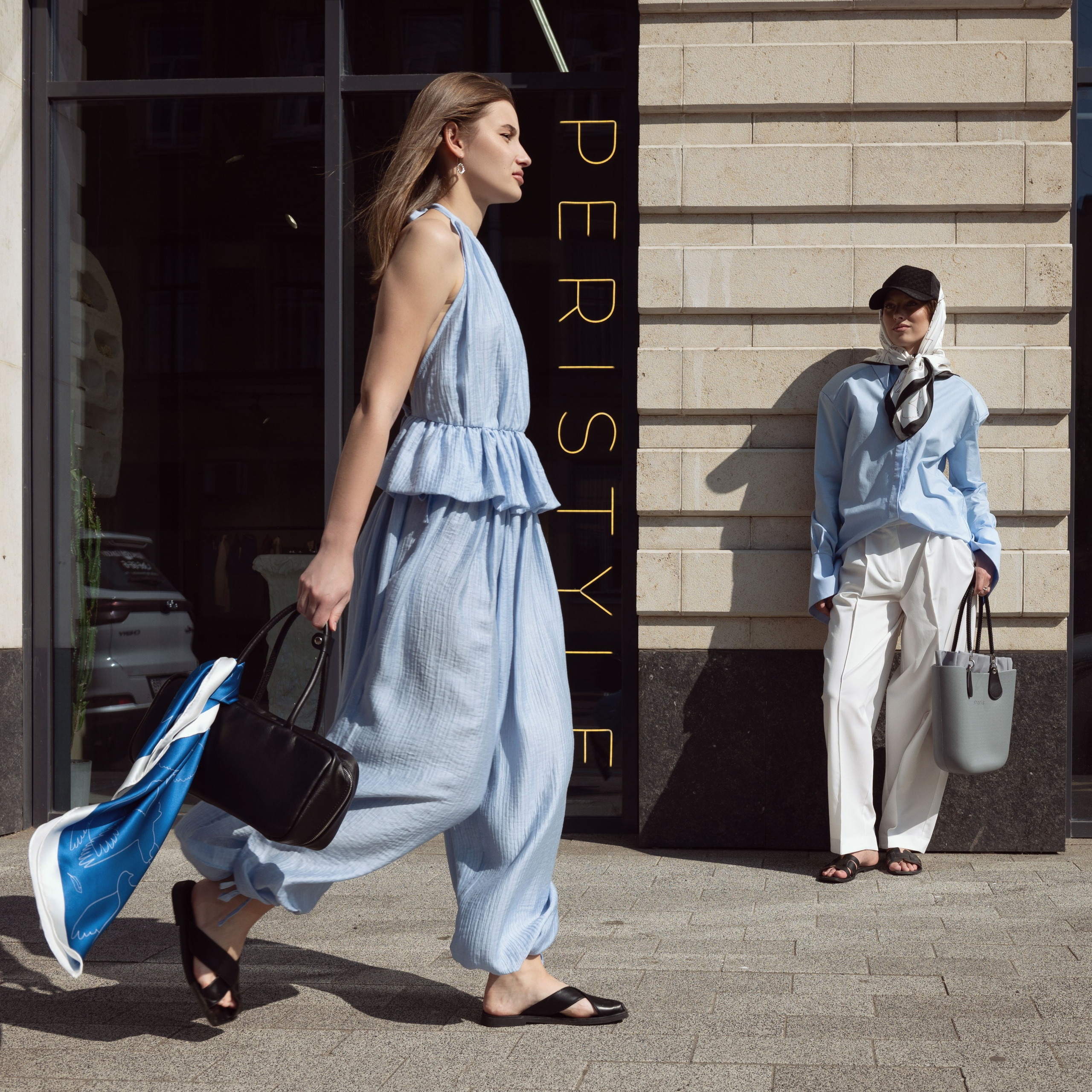 Девушка в голубых шароварах и голубом топе идет по улице, на ее суке повязан шелковый дизайнерский платок