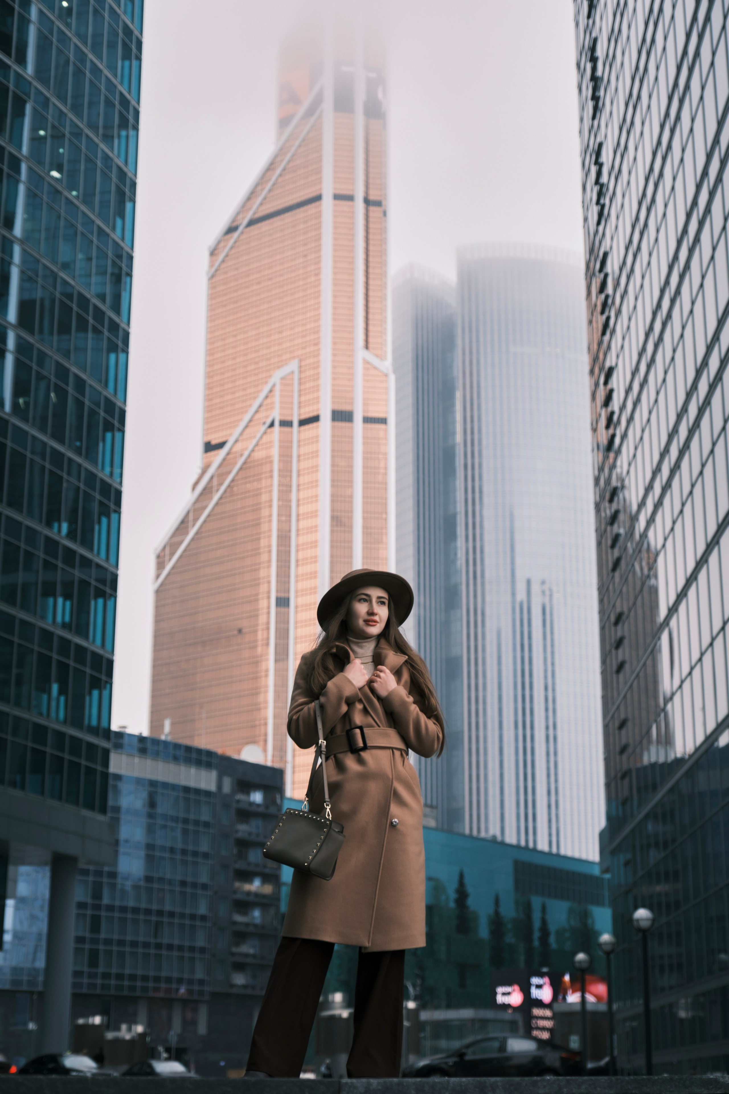Женская фотосессия в Москва-Сити: Девушка в полный рост позирует на фоне башни «Меркурий» и других небоскребов делового центра.