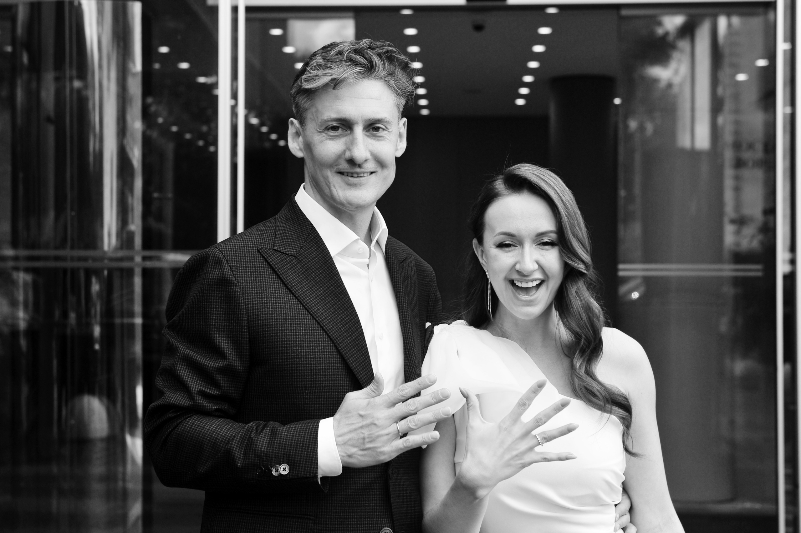 Свадьба в ЗАГСе Барвиха Luxury Village летом, молодожены вышли из ЗАГСа и демонстрируют обручальные кольца, чёрно-белое фото