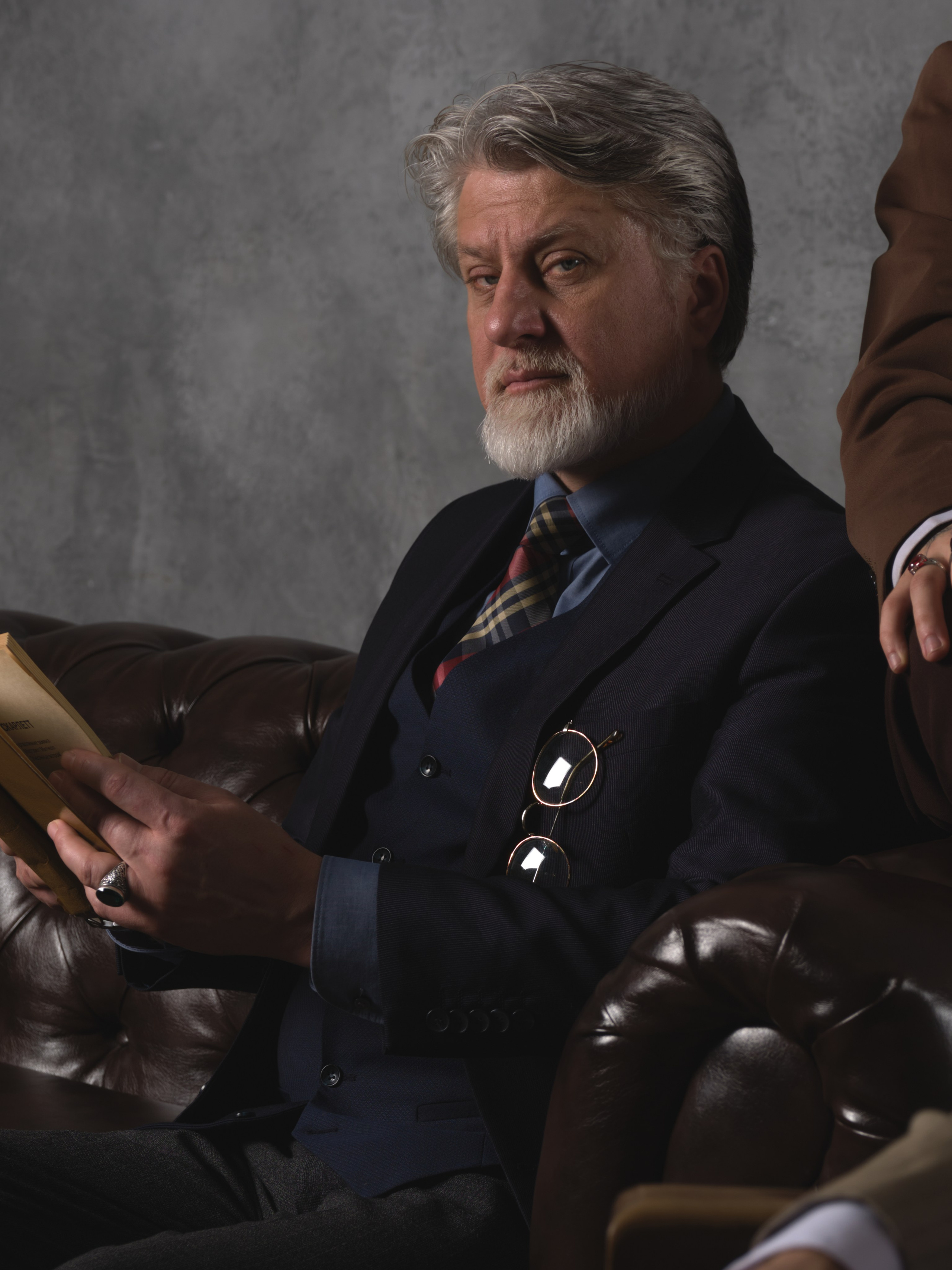 фотография взрослого мужчины в костюме который сидит на диване  и читает книгу