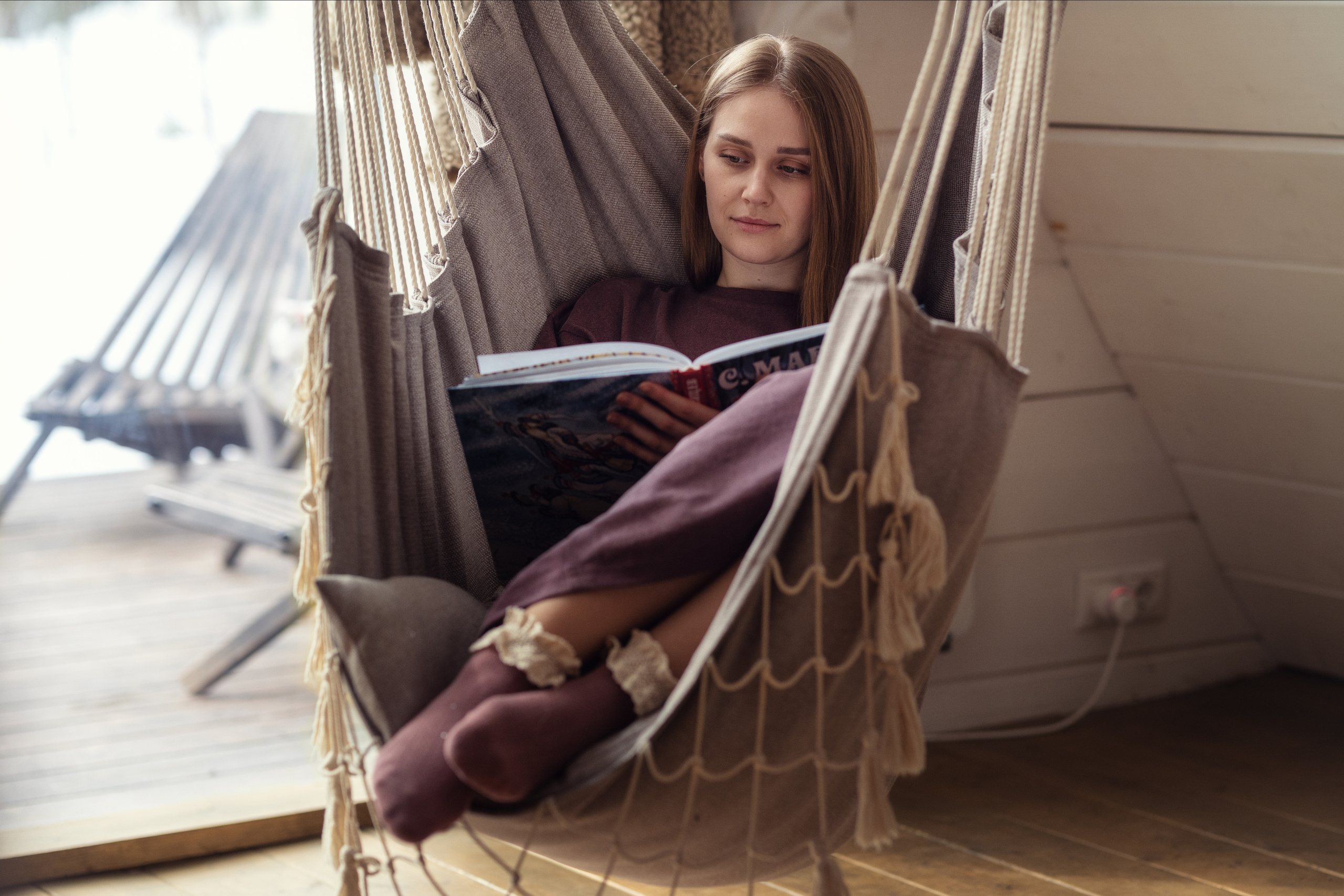 Девушка читает книгу в подвесных качелях-гамаке 