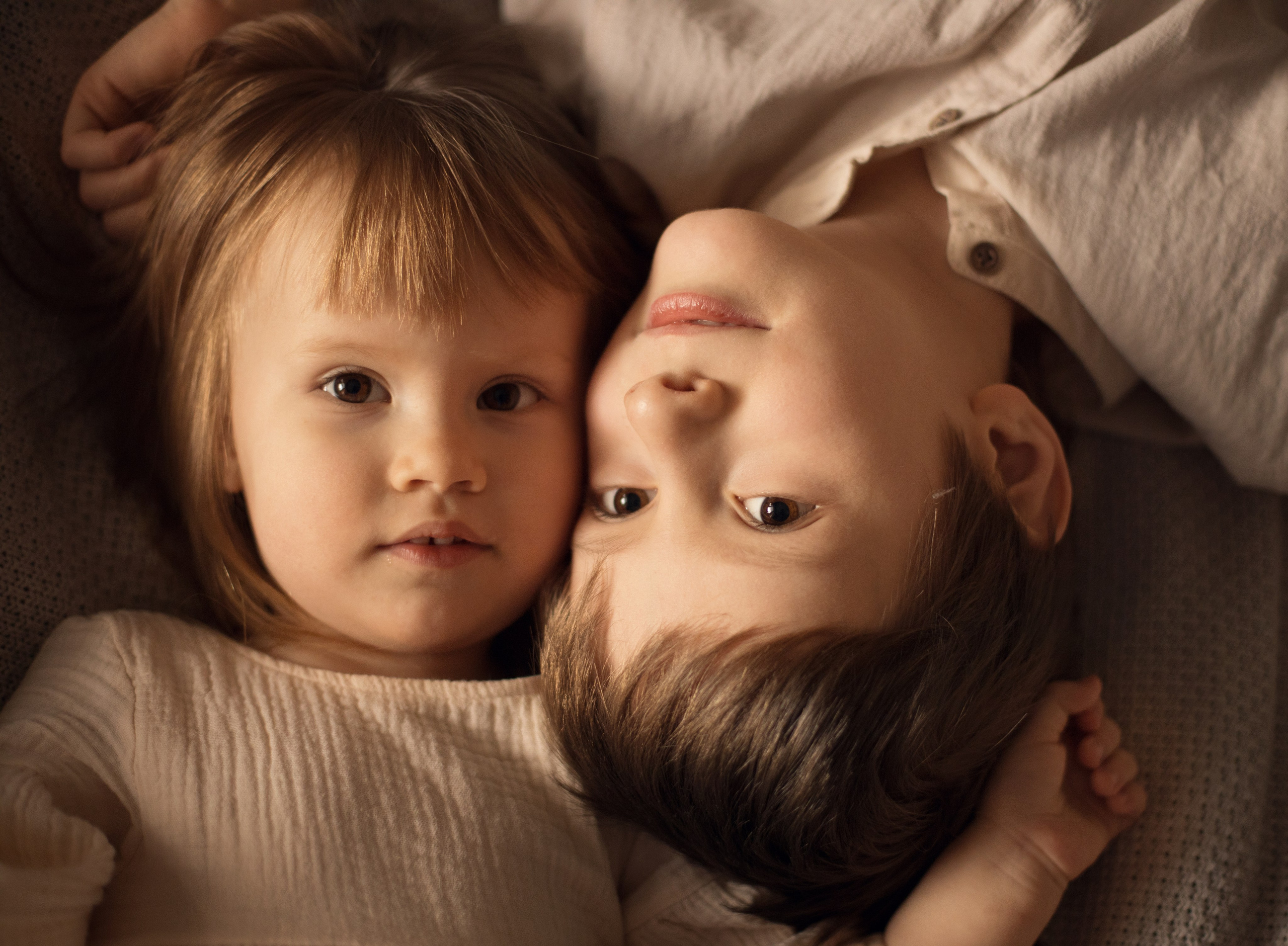 Портрет девочки и мальчика лёжа на диване в бежевых тонах