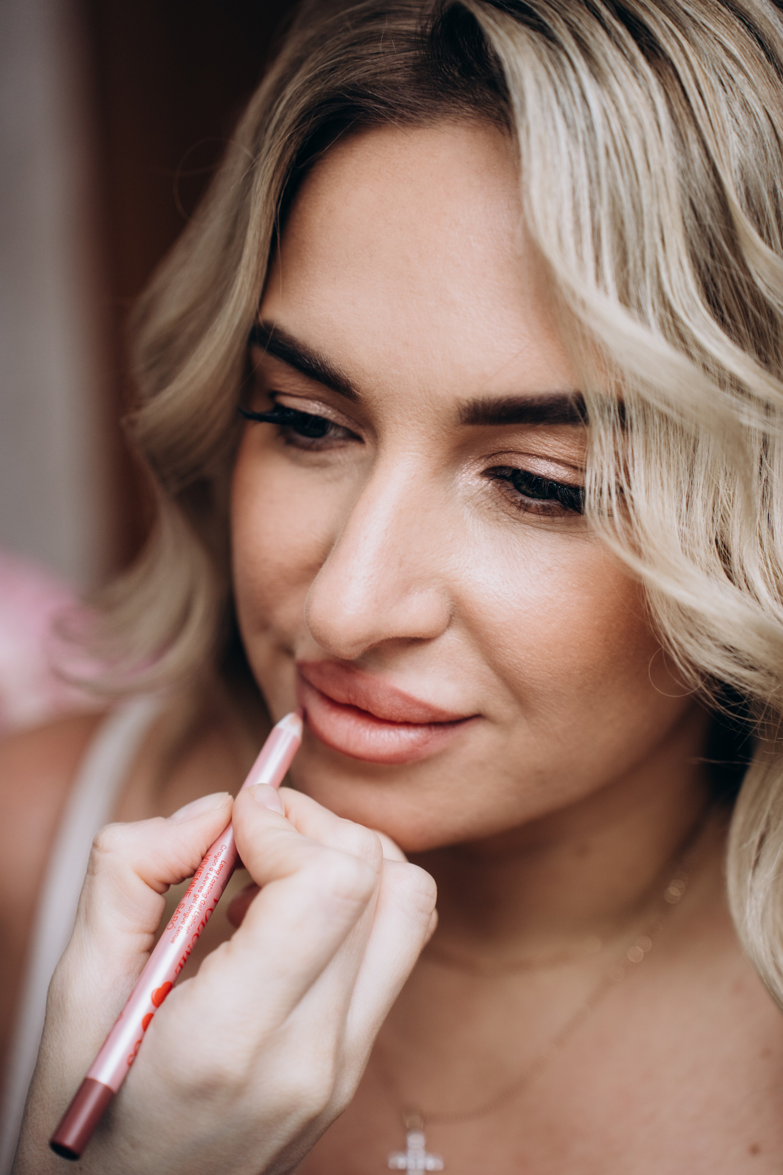 Невеста наносит макияж перед зеркалом — профессиональная фотосъемка свадебных сборов в Москве с вниманием к деталям.