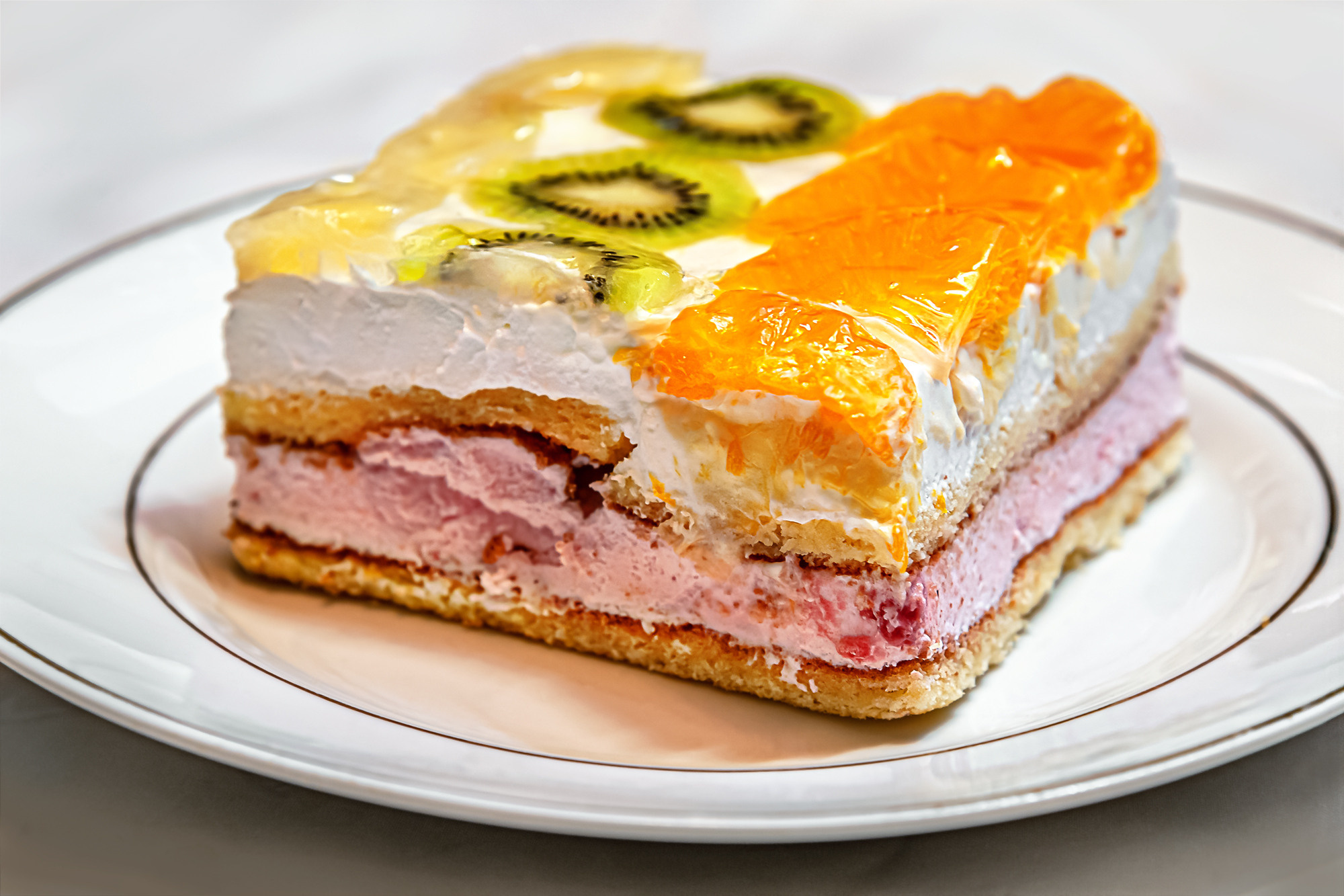 biscuit cake with a layers of home-made cottage cheese decorated with tropical fruits on a white porcelian plate