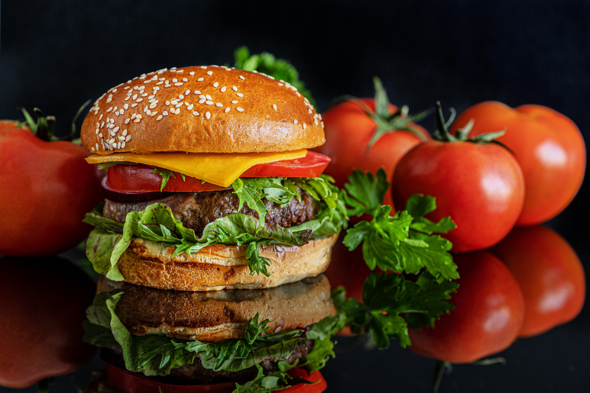 burger with cheese, tomatoes, chard and arugula on a black glass surface