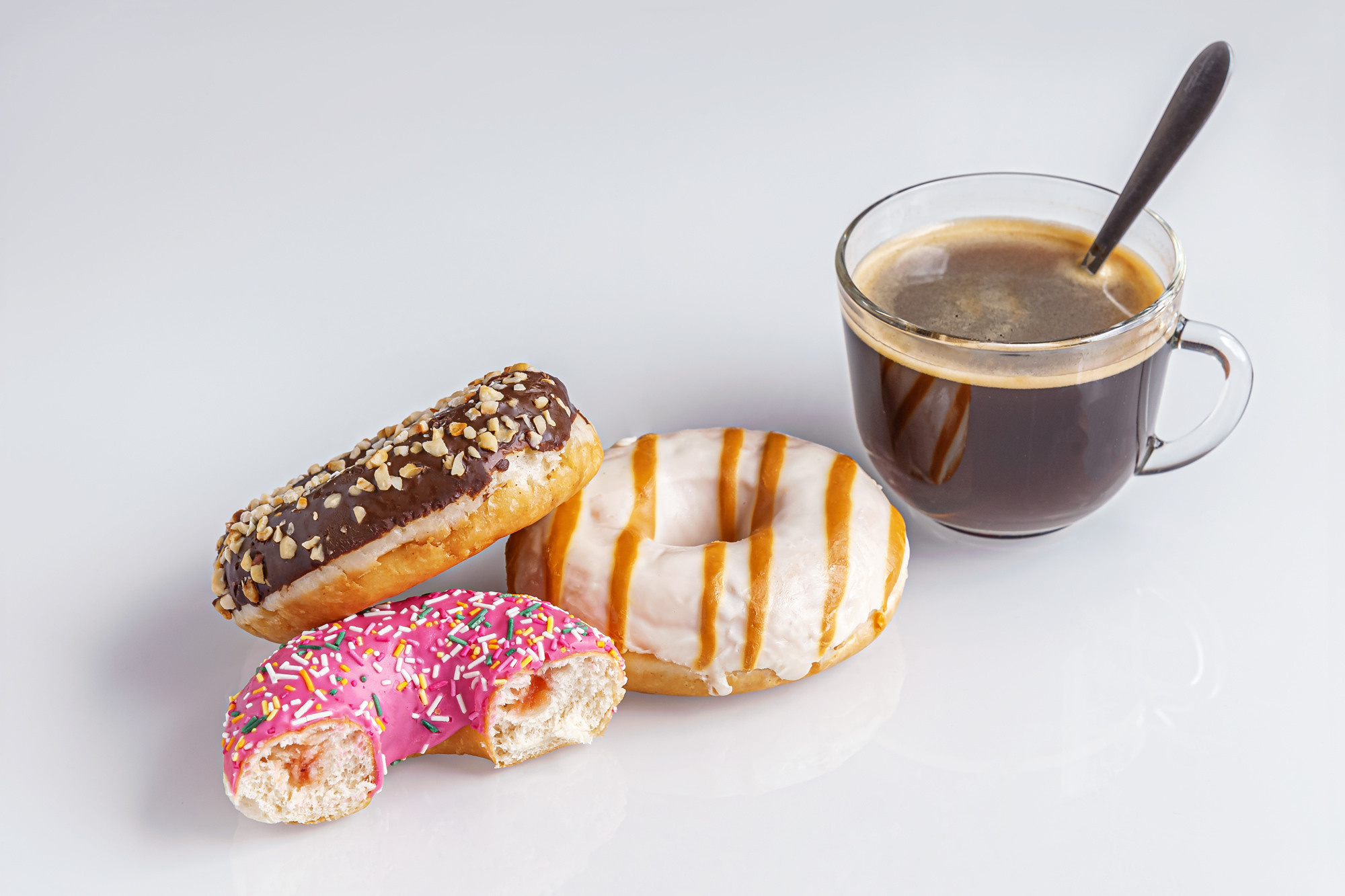 freshly baked chocolate, caramel and strawberry donuts and a cup of coffee on a white glass surface