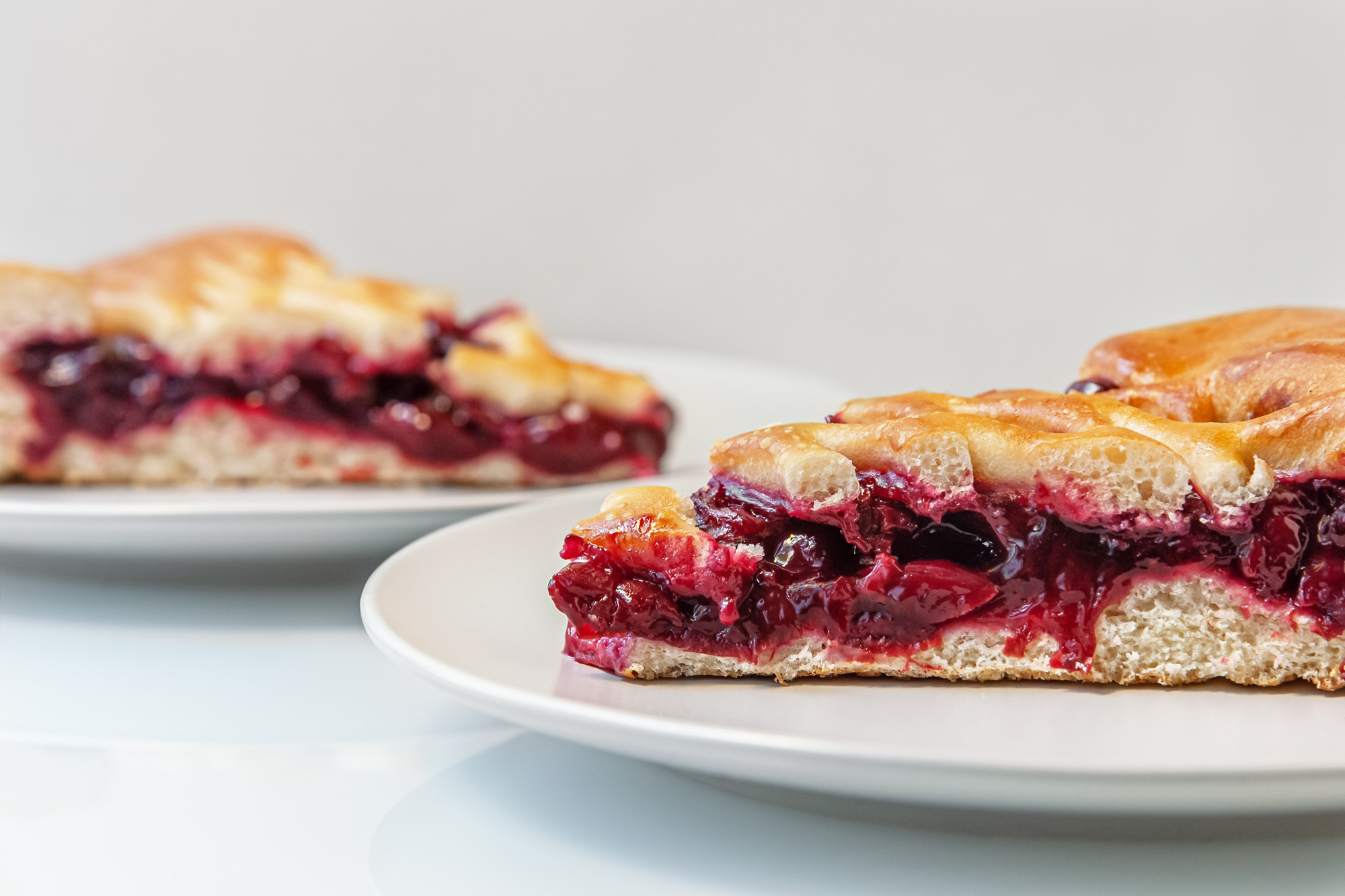 white ceramic plates with sliced cherry pie on a light glass surface