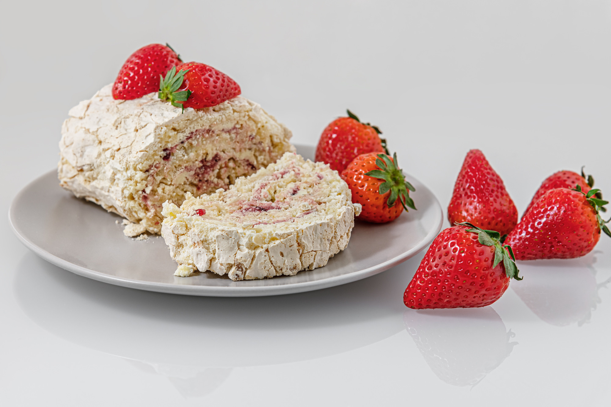 delicious meringue roll with strawberry cream and fragrant ripe strawberries on a white glass surface