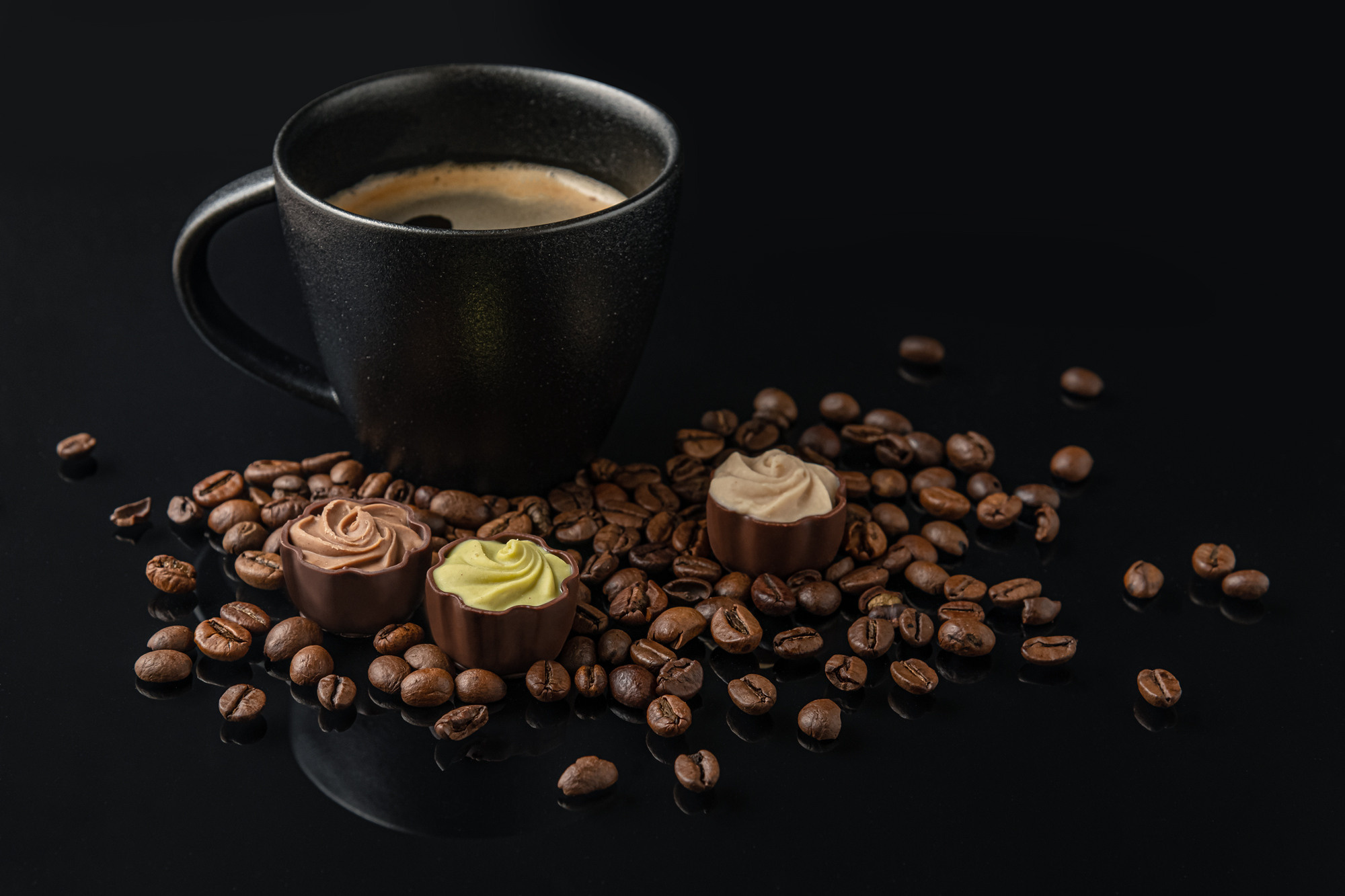 aromatic freshly brewed coffee in a black ceramic cup, coffee beans and gourmet chocolate sweets