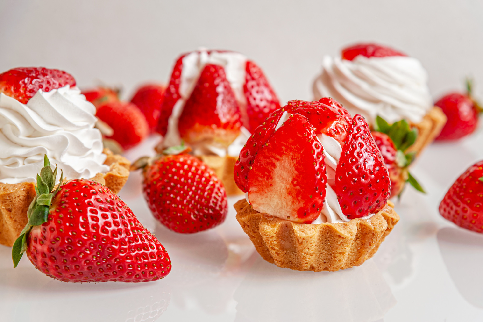 gourmet tartlets with whipped cream and fragrant juicy strawberries on a glass surface
