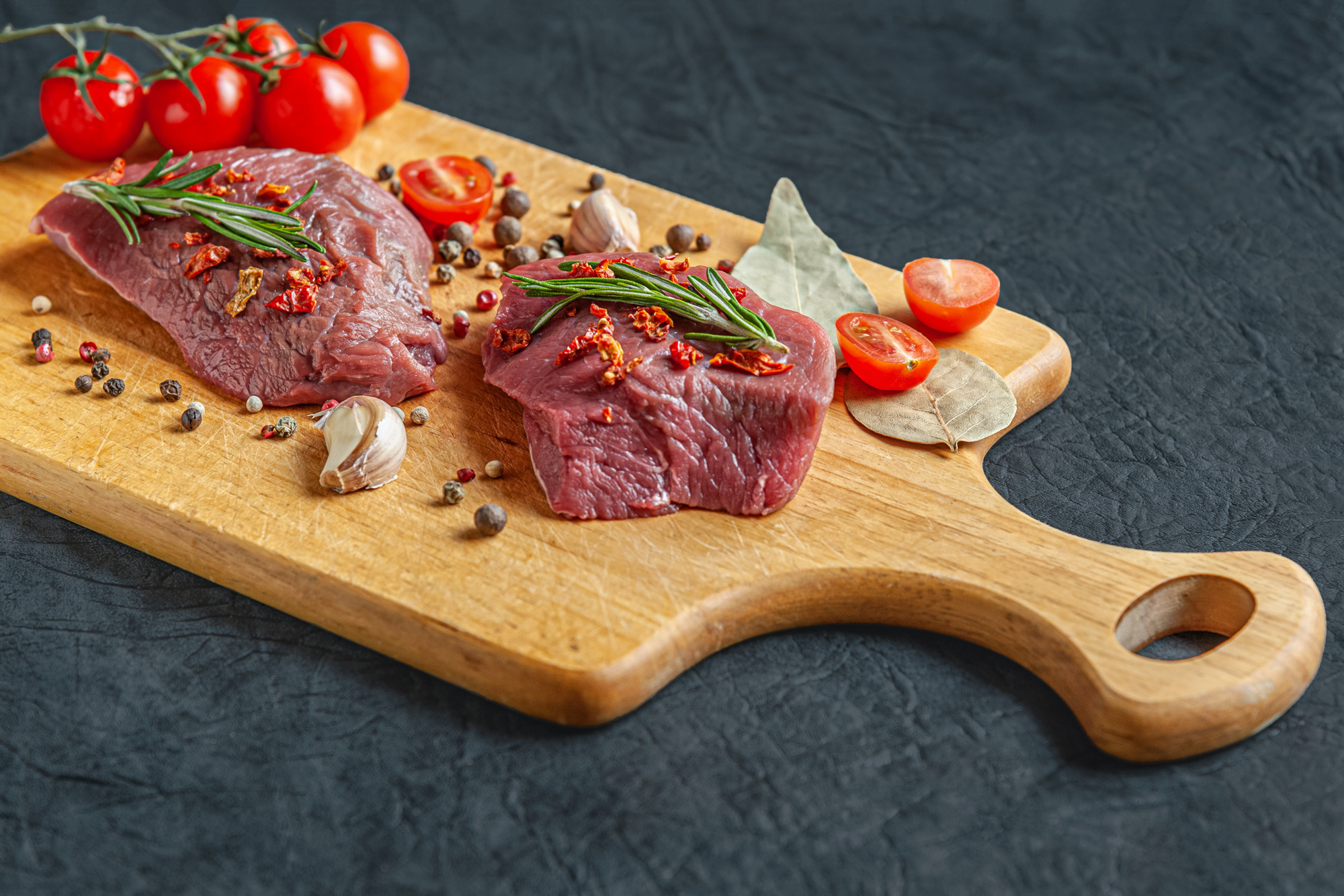 raw meat with spices, cherry tomatoes and garlic on a wooden cutting board