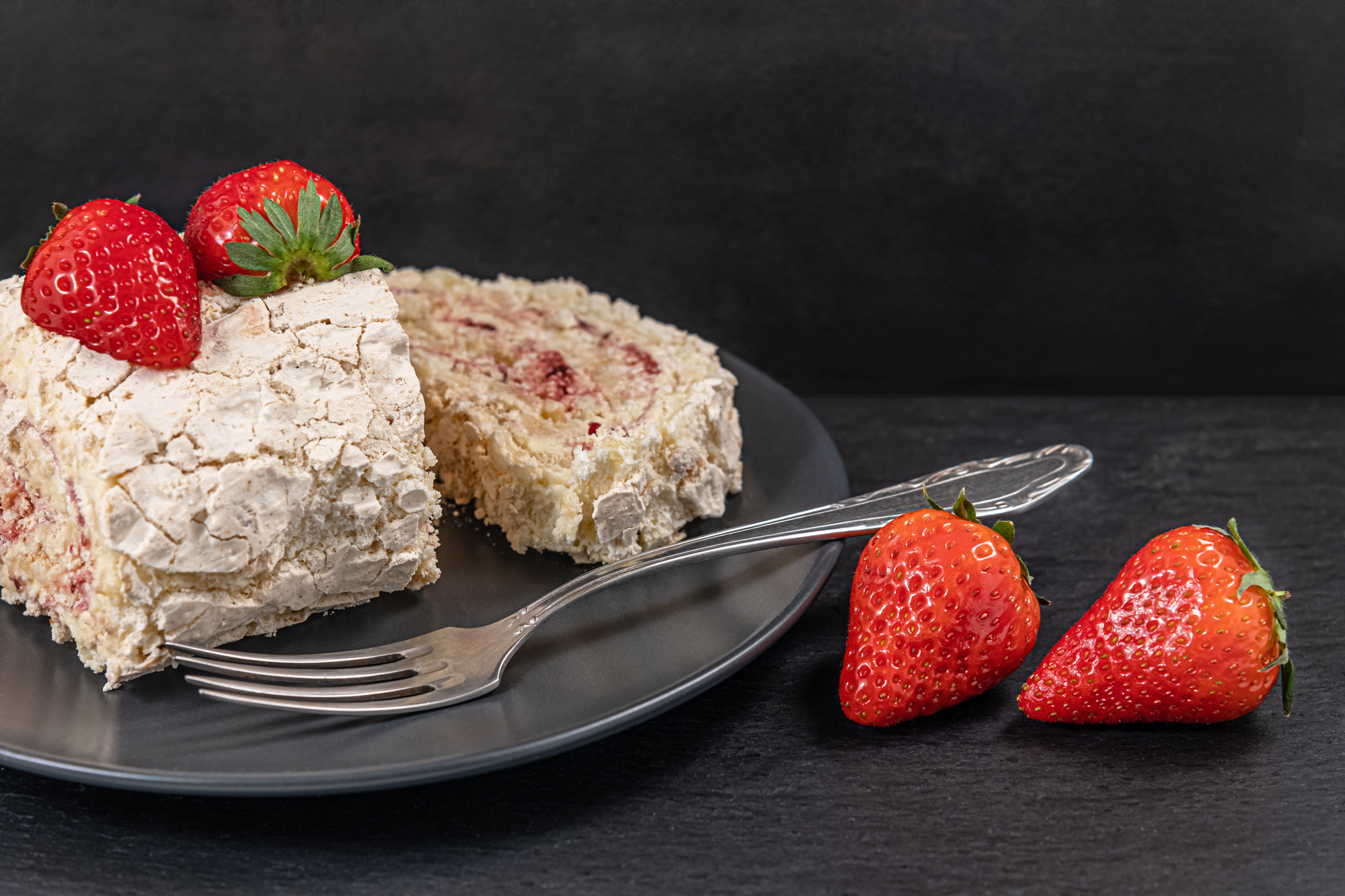 delicious meringue roll with strawberry cream on a black slate surface