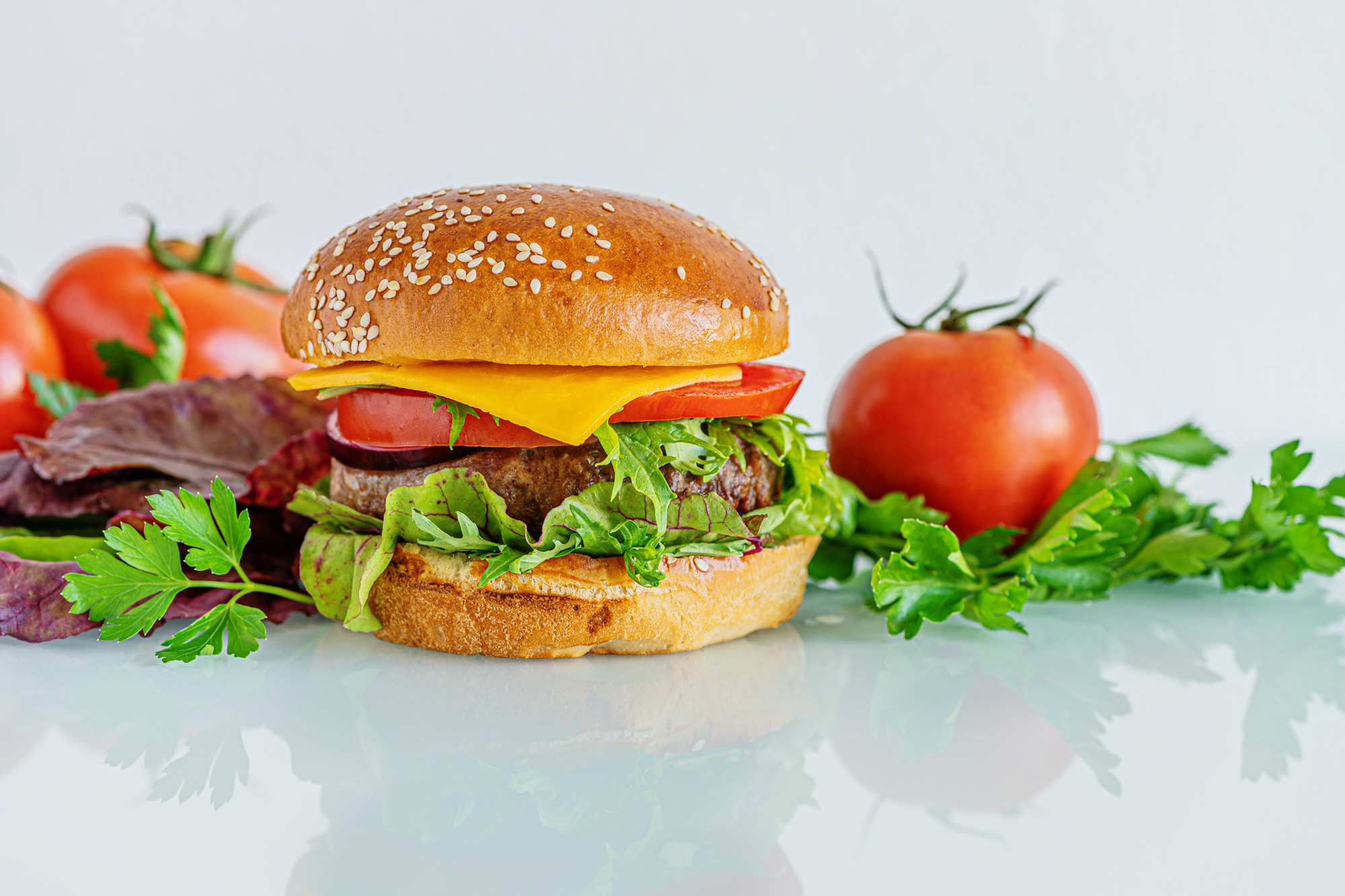 burger with cheese, tomatoes, chard and arugula on a white glass surface